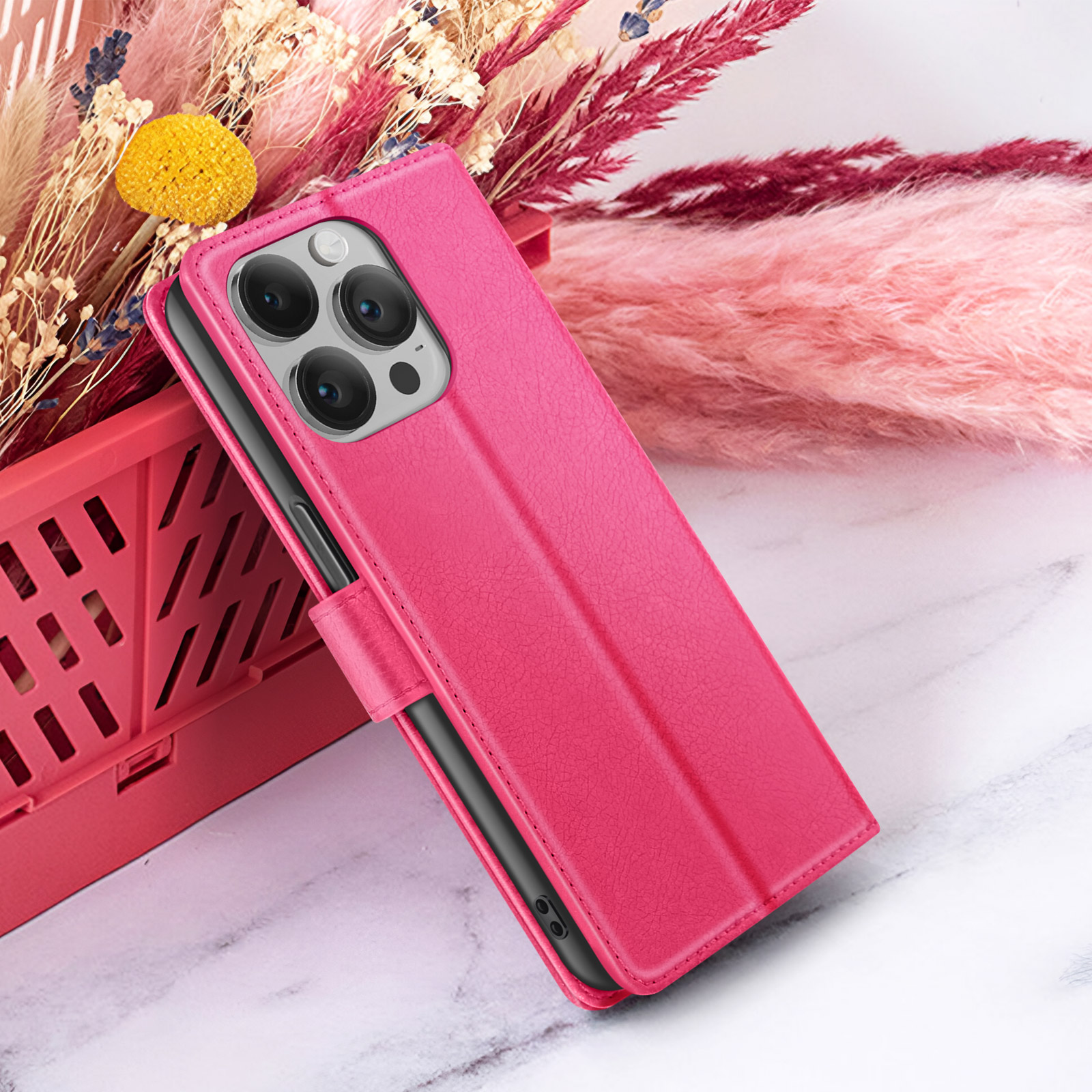 Een roze telefoonhoesje met een telefoon erin, rustend op een marmeren oppervlak, met bloemen op de achtergrond.