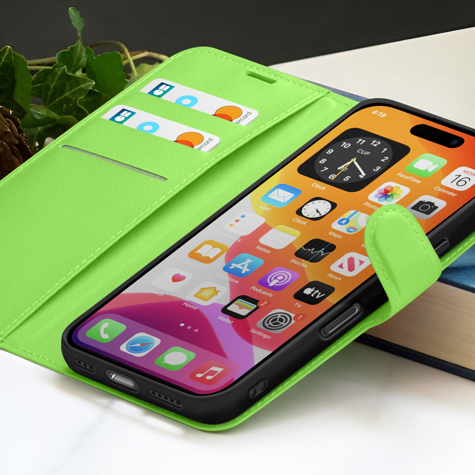Een iPhone in een groene hoes toont app-iconen. Twee creditcards zijn zichtbaar in de hoes. Een boek staat op de achtergrond.