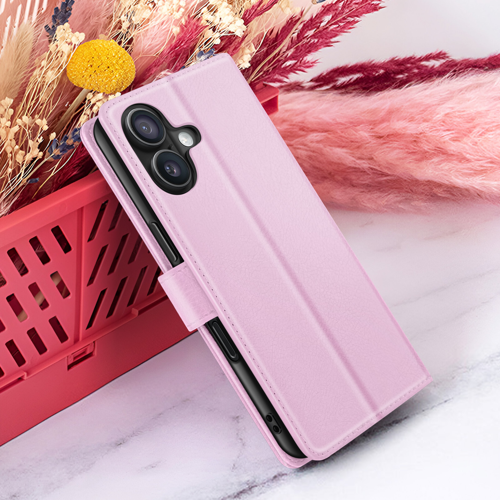 Een roze telefoonhoesje ligt op een rode doos. Gedroogde bloemen op de achtergrond. De hoes heeft cameralenzen.