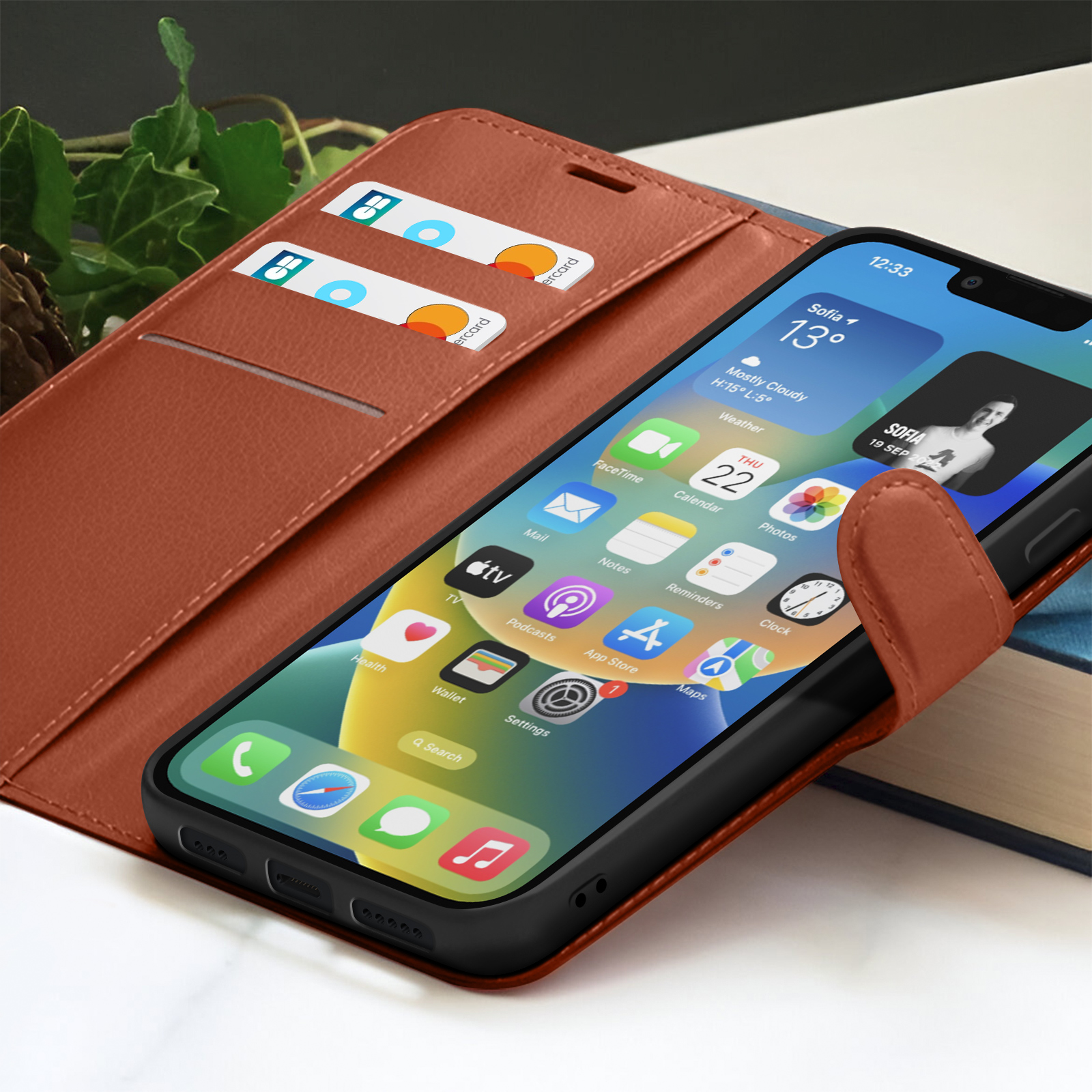 Een iPhone in een bruine leren hoes. Creditcards zijn zichtbaar. Het scherm toont apps en een weerwidget met Sofia.