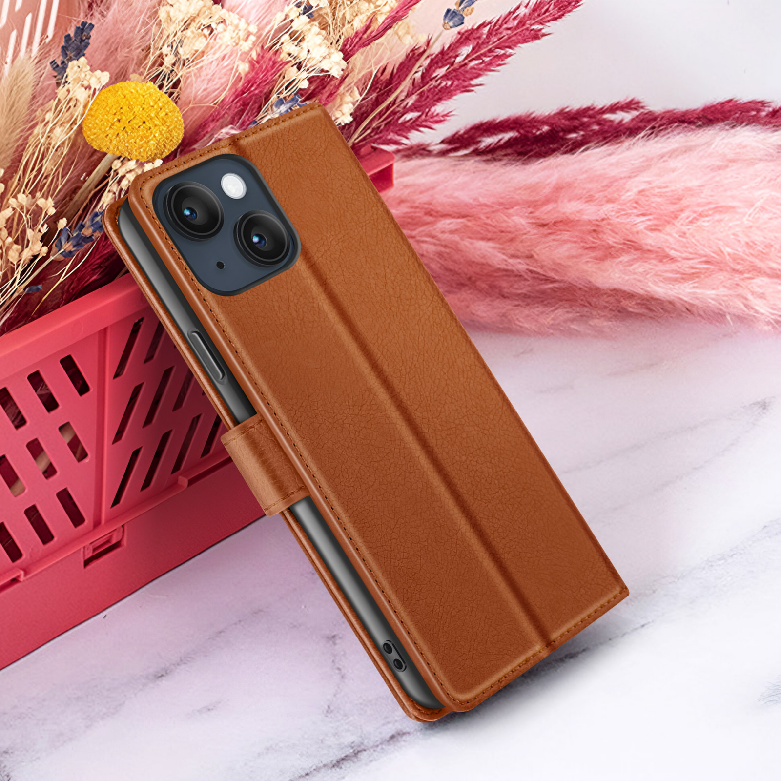 Een bruine leren telefoonhoes wordt getoond, gedeeltelijk open, met een telefoon erin. Achter, roze bloemen en een rode container.