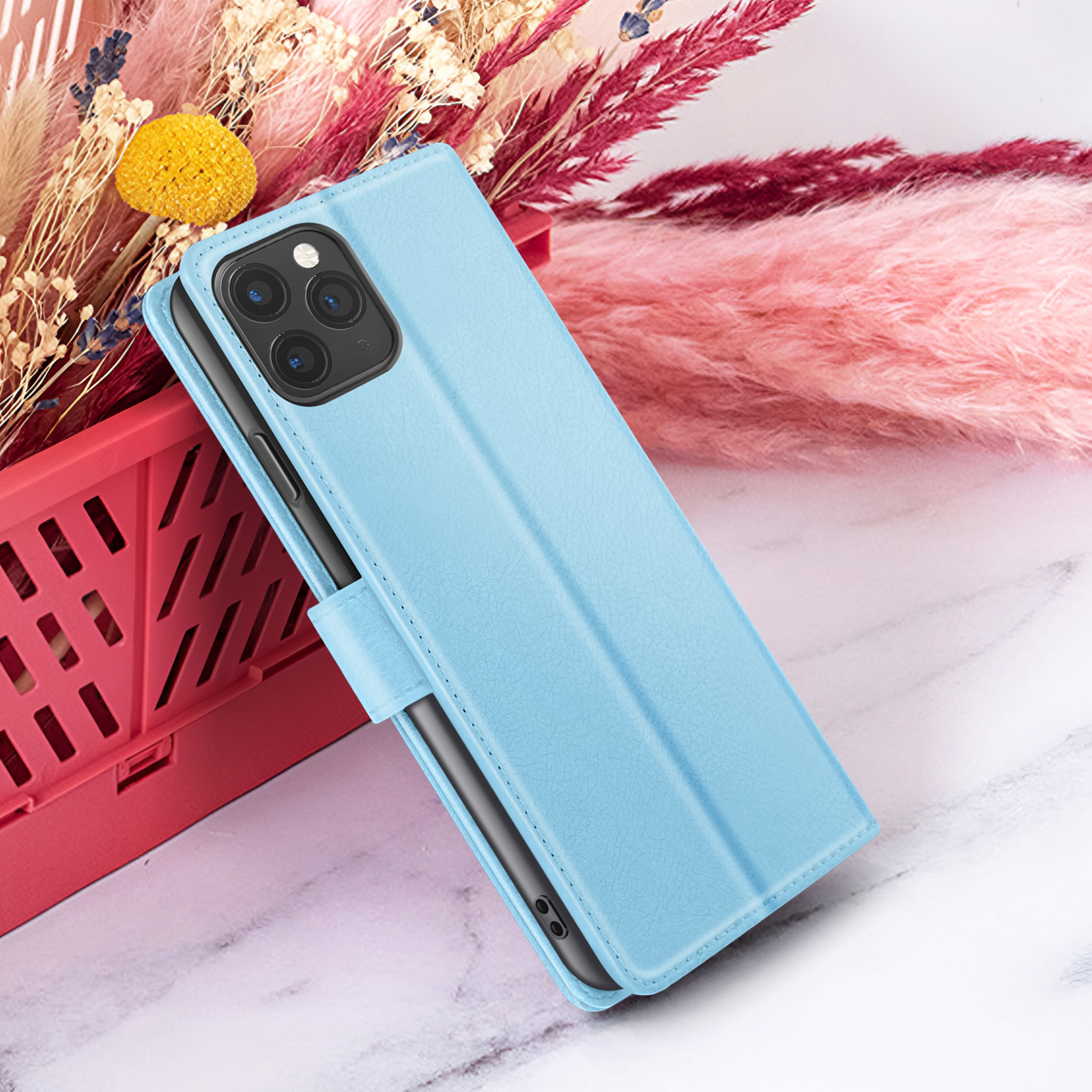 Un étui de téléphone bleu clair avec un téléphone à l'intérieur se trouve devant des fleurs roses et un panier rouge.