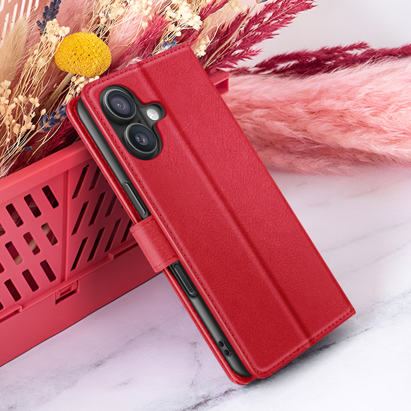 Een rode telefoonhoes is open en onthult een telefoon met twee camera's. Het staat in de buurt van roze en rode gedroogde bloemen.