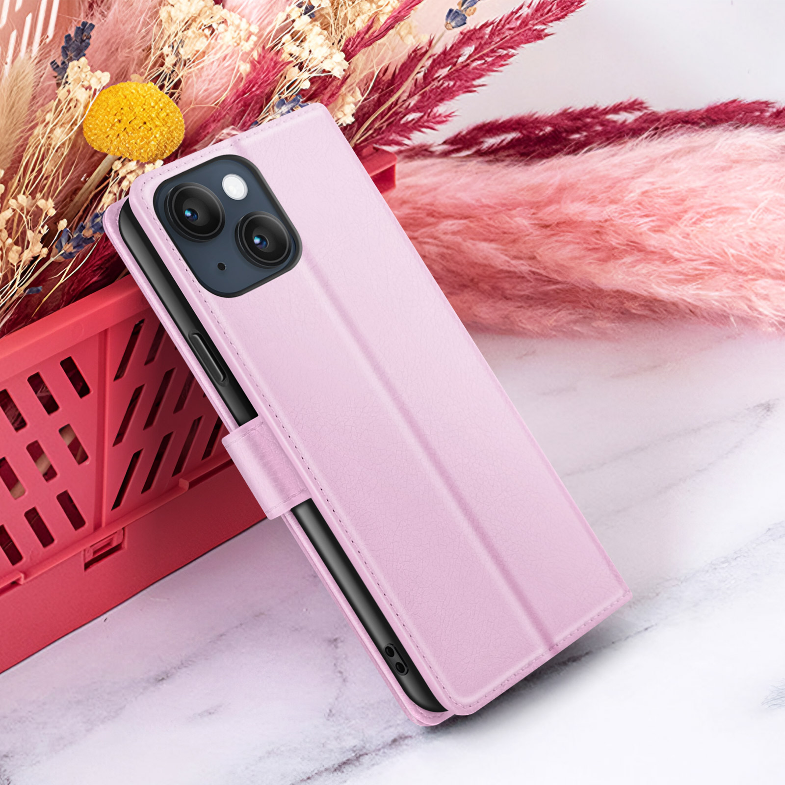 Een roze telefoonhoesje op een marmeren oppervlak. Achter, roze en rode pluizige decoraties en droogbloemen.