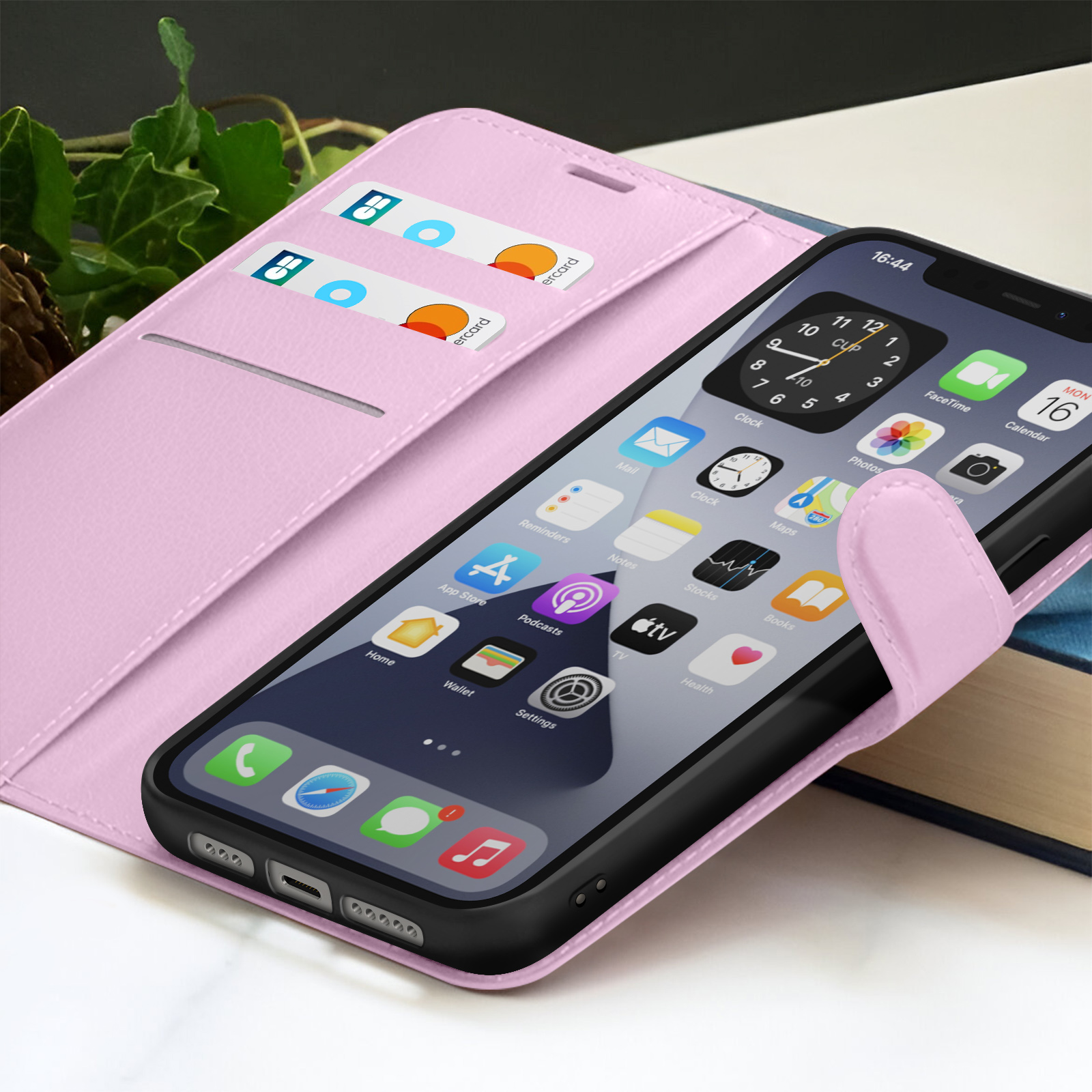 Een smartphone in een roze hoesje met de tijd, apps en creditcards op de cover. Klimopbladeren en een boek zijn zichtbaar op de achtergrond.