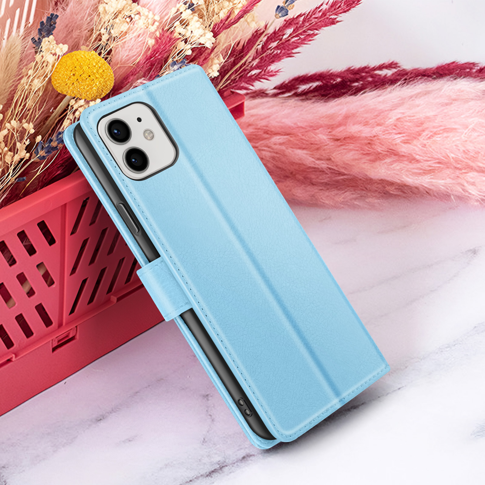Een blauwe telefoonhoes, open, ligt op een marmeren oppervlak. Achtergrond: roze en beige gedroogde bloemen, rode doos.