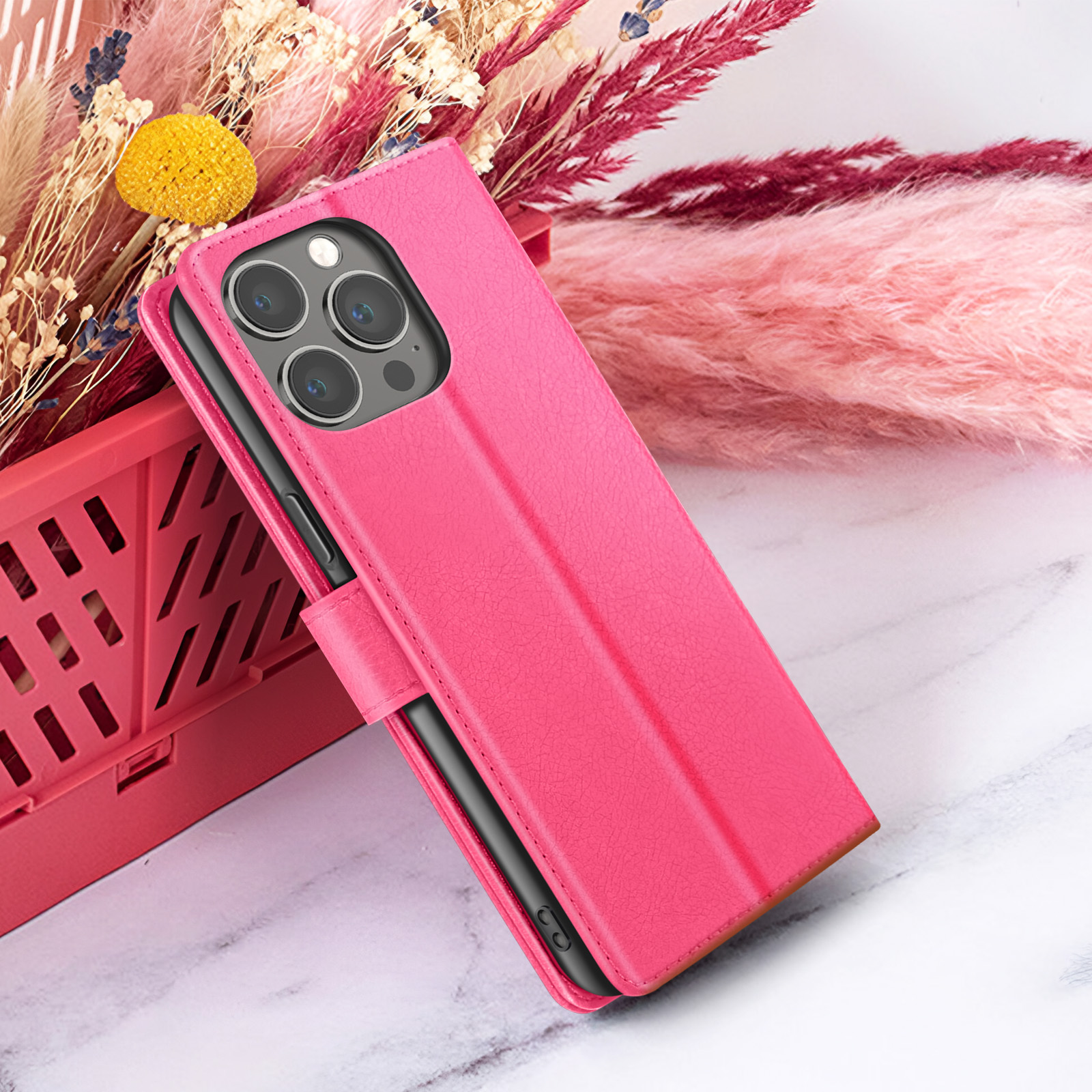 Een roze telefoonhoesje met een telefoon erin wordt getoond op een marmeren oppervlak met decoratieve bloemen op de achtergrond.