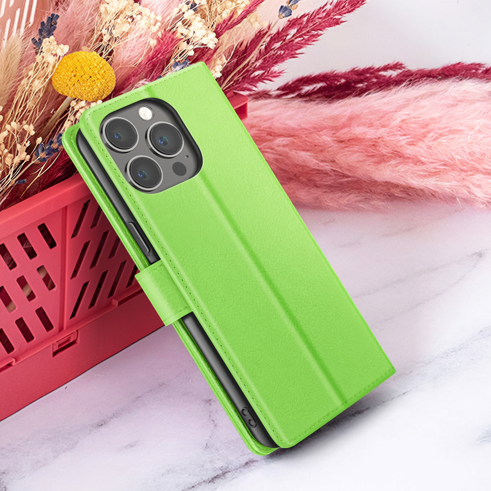 Een groene telefoonhoes is open en toont een telefoon. Roze en rode bloemen op de achtergrond, met een rode container.