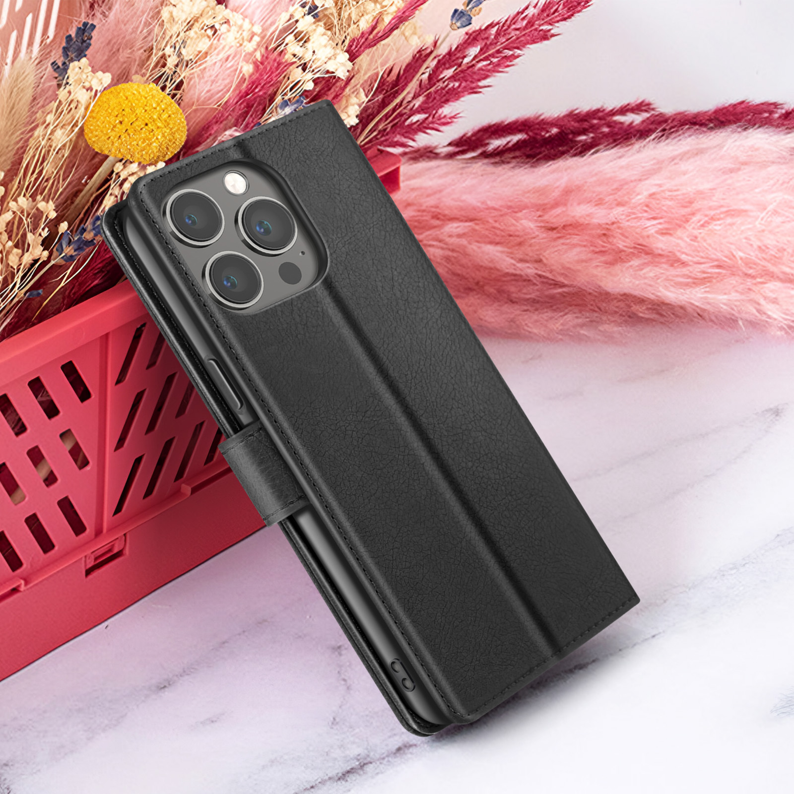 Een zwarte leren telefoonhoes met een telefoon erin, rustend op een marmeren oppervlak, met bloemen op de achtergrond.