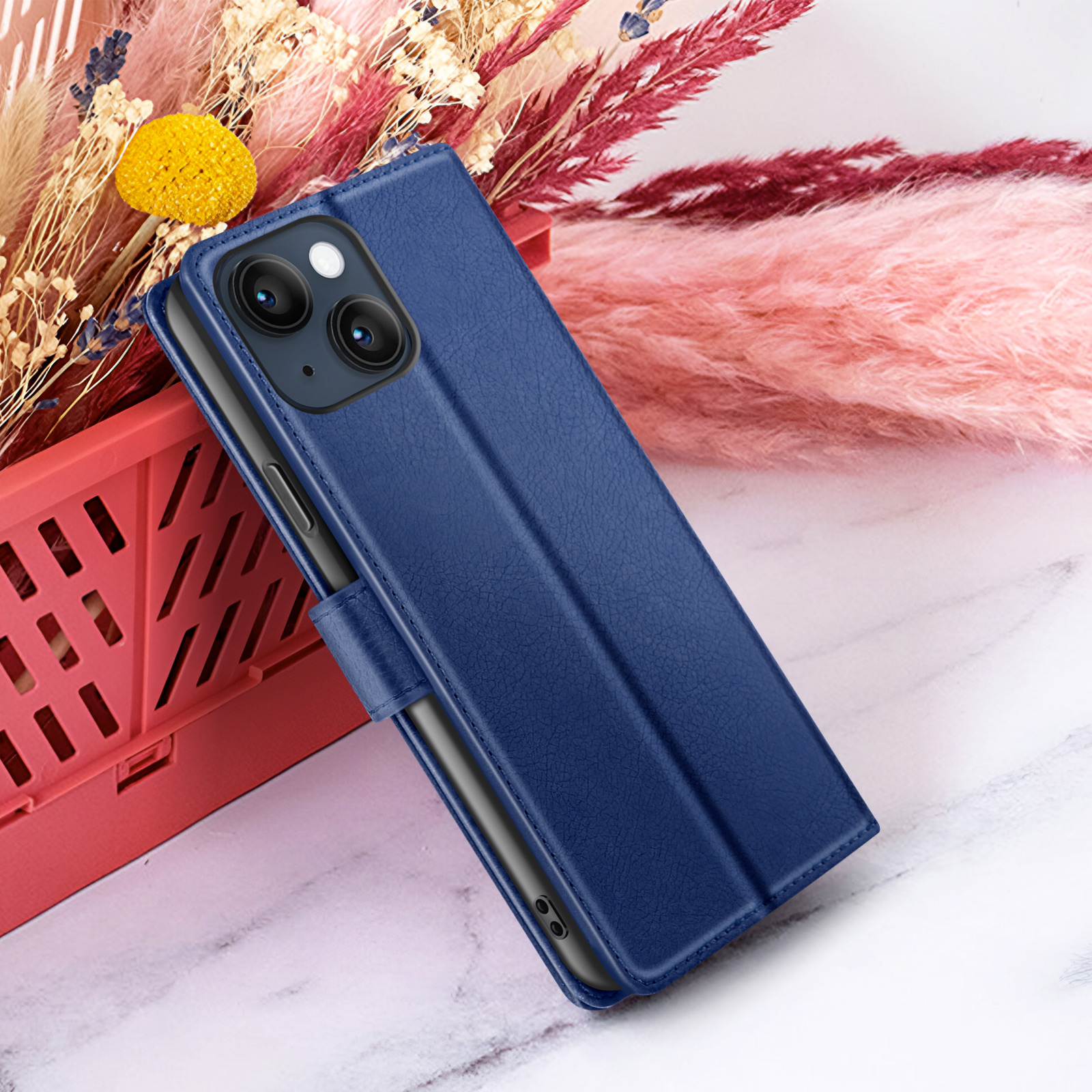 Een blauwe telefoonhoes is open, met een telefoon erin. Bloemen en een rode mand op de achtergrond.