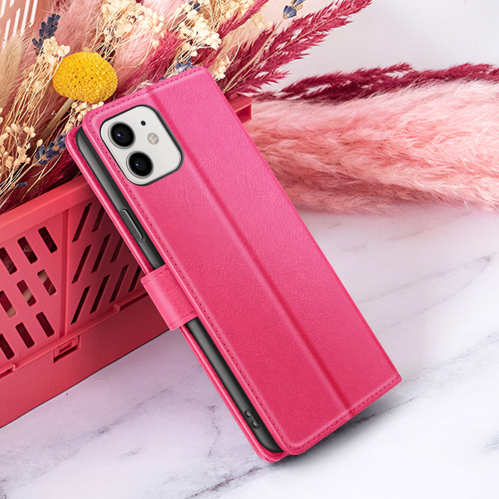 Een fuchsia telefoonhoesje met portemonnee-ontwerp ligt op een marmeren oppervlak naast droogbloemen.