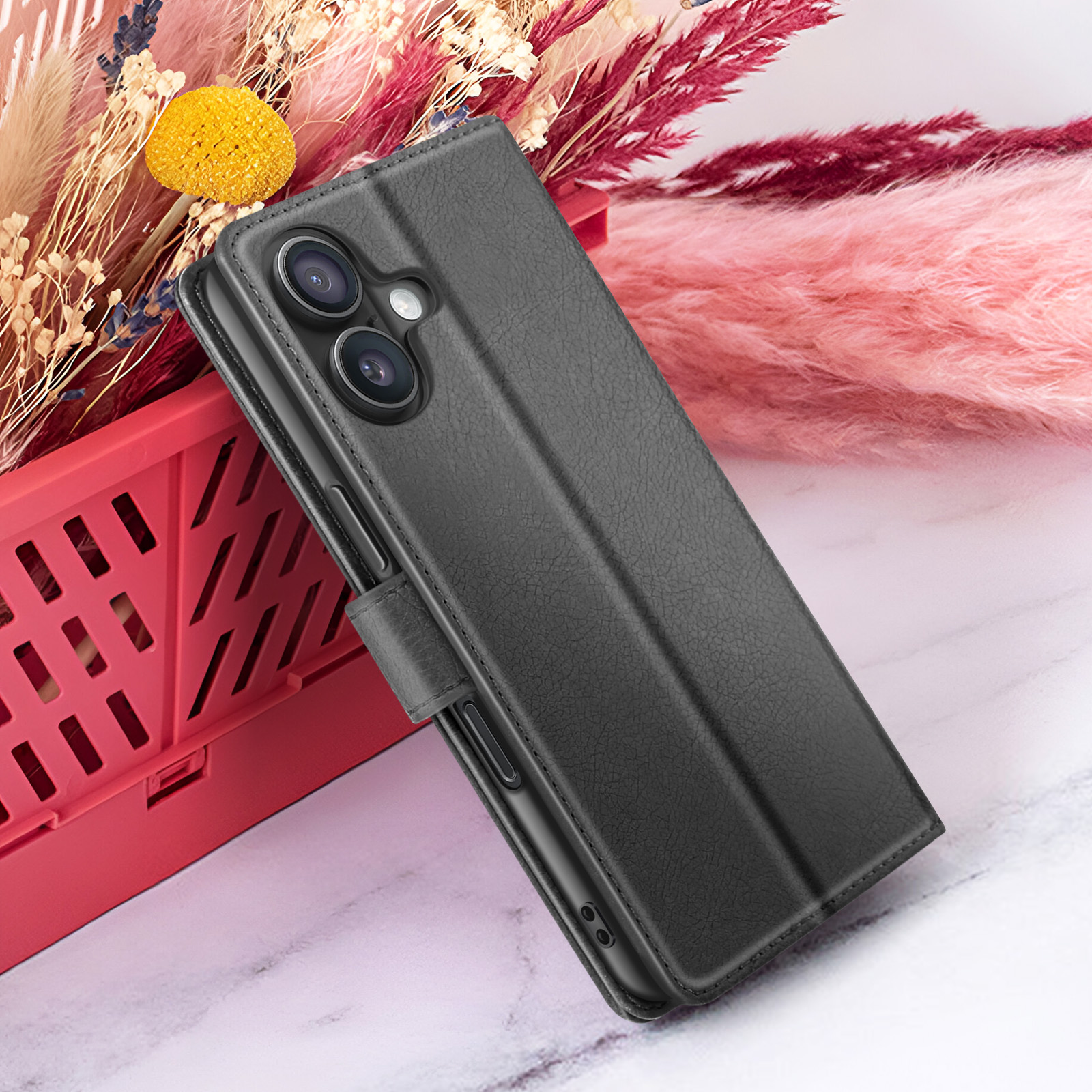 Een zwarte telefoonhoes met camera ligt op een rode krat, met bloemen op de achtergrond. De hoes ligt op marmer.