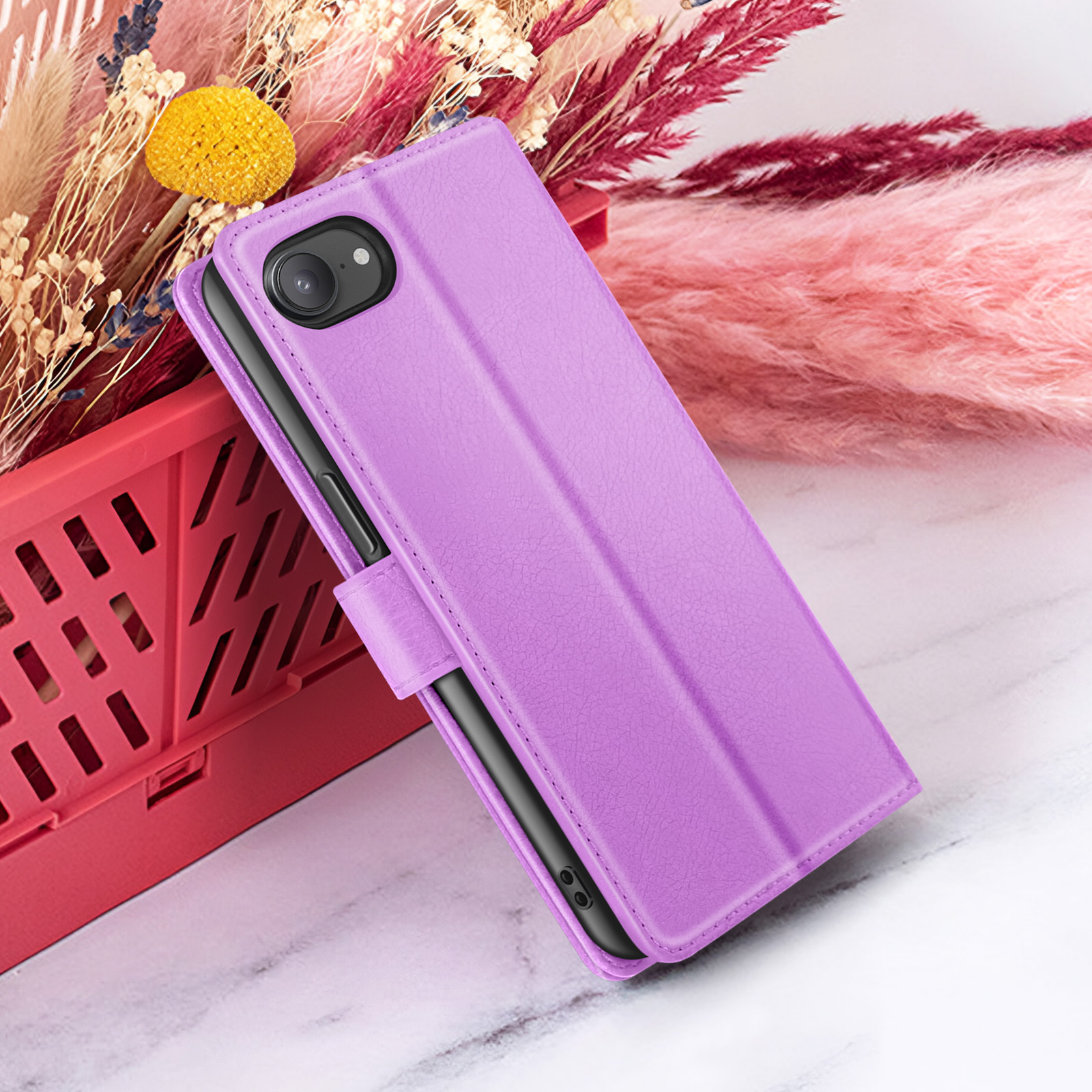 Een paarse telefoonhoes ligt op een marmeren oppervlak, met bloemen op de achtergrond en een rode mand. De telefoon is zichtbaar.