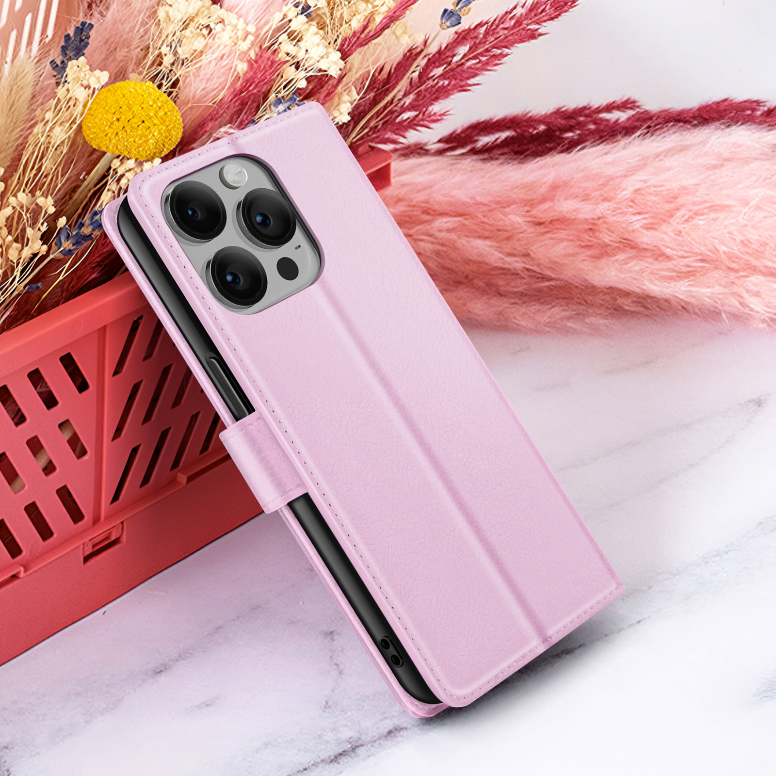 Una funda de teléfono rosa, que sostiene un teléfono, está abierta. El fondo incluye flores rosas, blancas y amarillas y una caja roja.