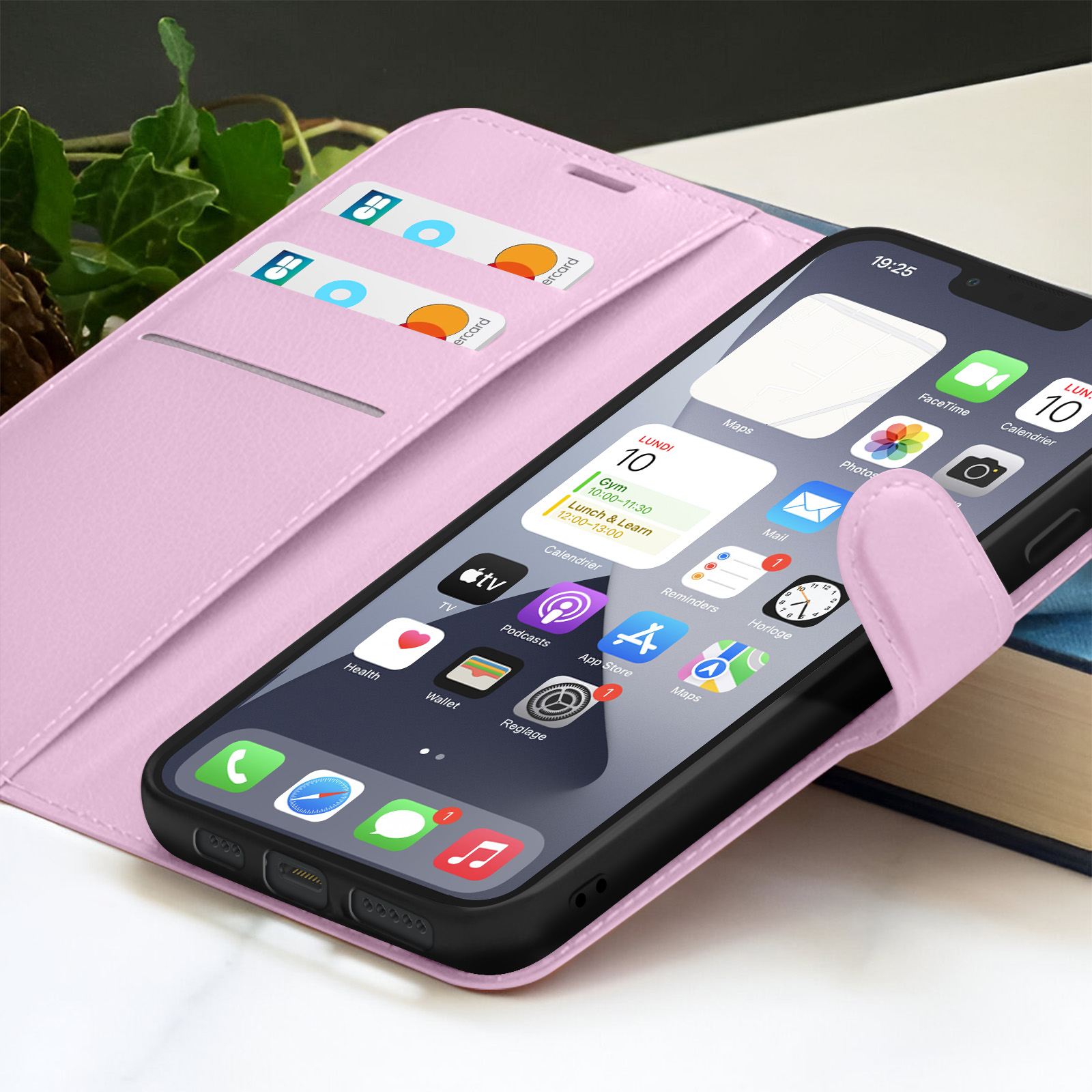 Een iPhone in een roze hoesje met kaarten. Het scherm toont apps. De achtergrond heeft gebladerte en een boek.
