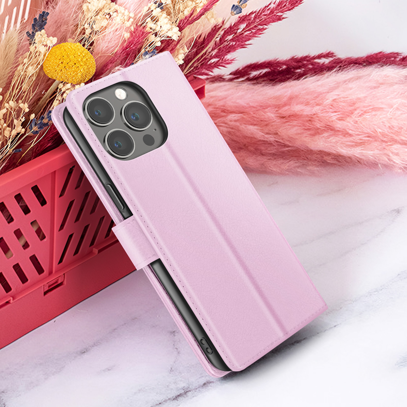 Roze telefoonhoes met telefoon, tegen gedroogde bloemen en marmer.