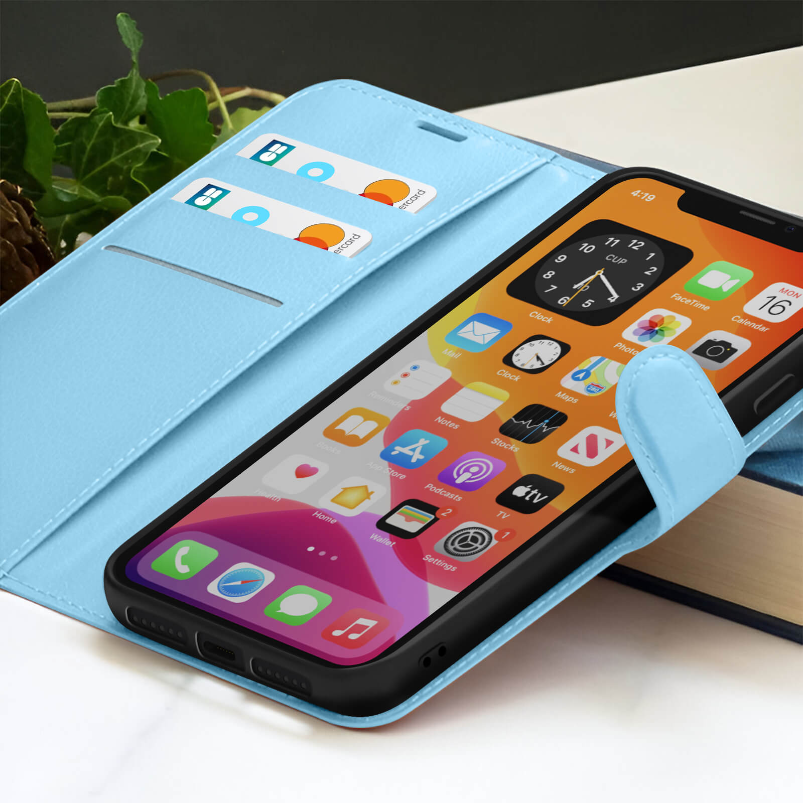 Een telefoon in een blauwe hoes met creditcards. De telefoon toont app-iconen en een klok. De hoes ligt op een boek.