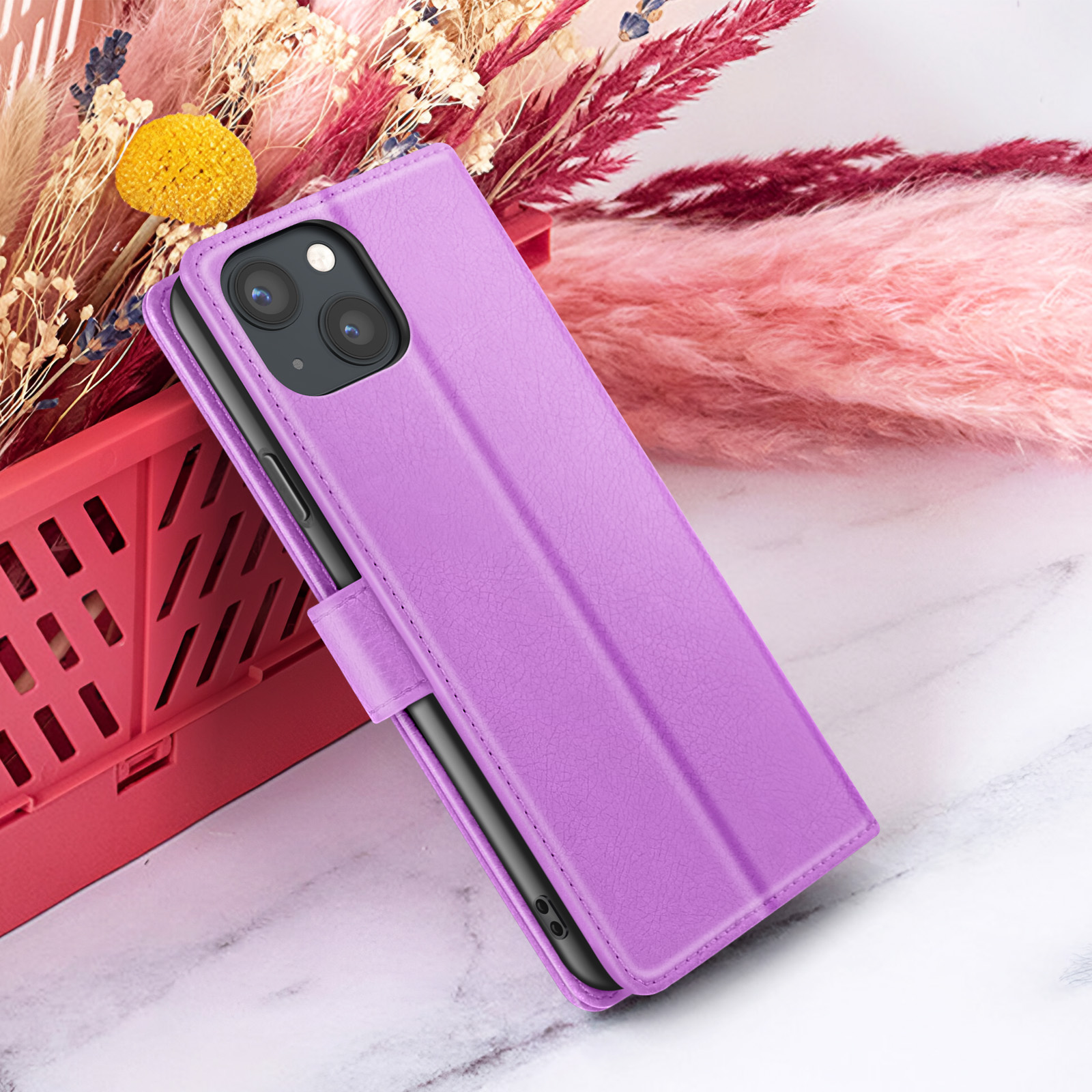 Een paarse telefoonhoes met een iPhone erin, geplaatst voor bloemen en een roze oppervlak.