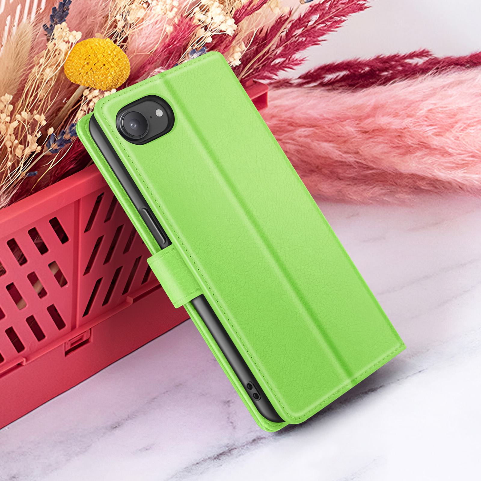 Een groene telefoonhoes staat open. Bloemen en een rode container op de achtergrond. De hoes ligt op een marmeren oppervlak.