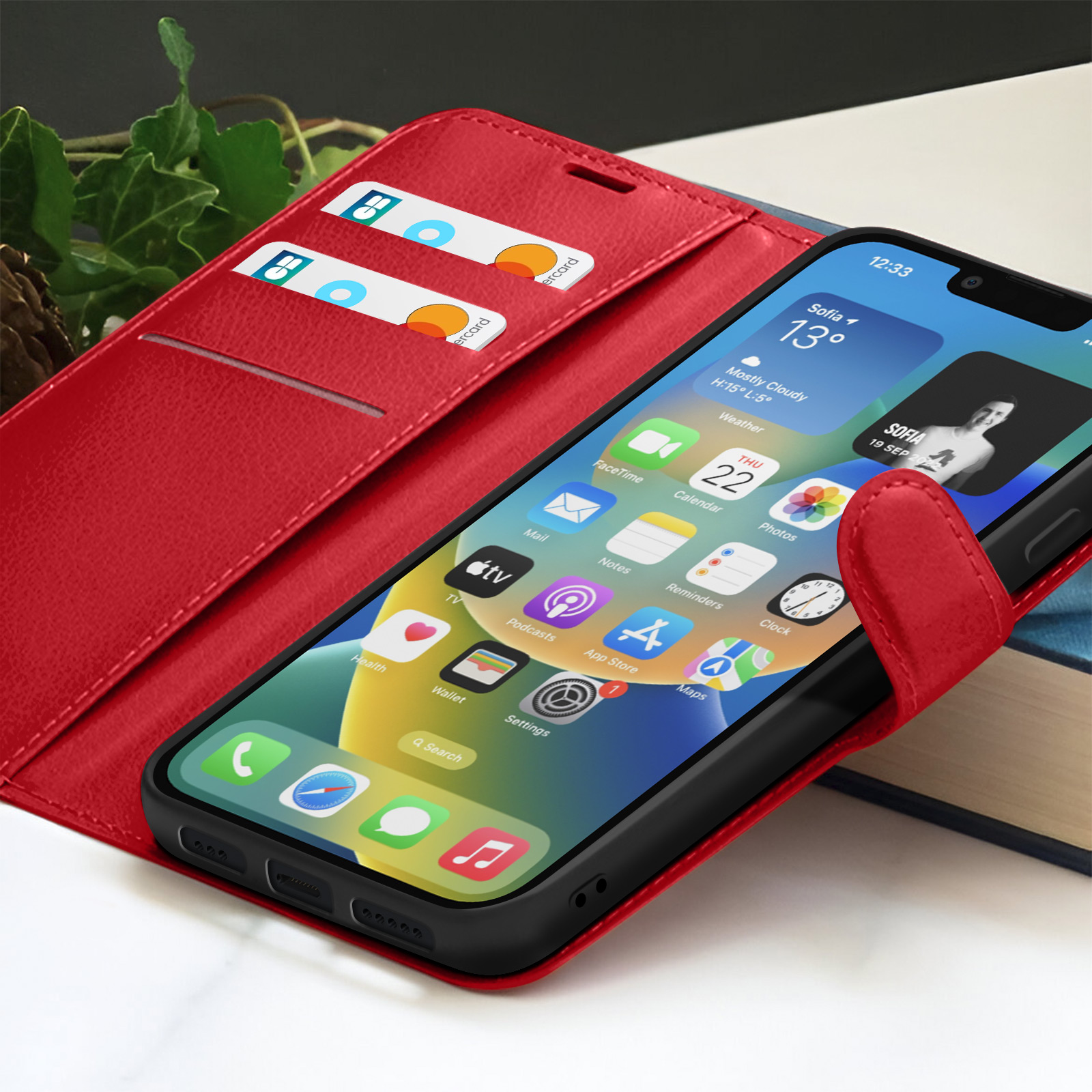 Een iPhone in een rode hoes wordt getoond. Het scherm toont apps en een weerwidget. Creditcards in een sleuf.