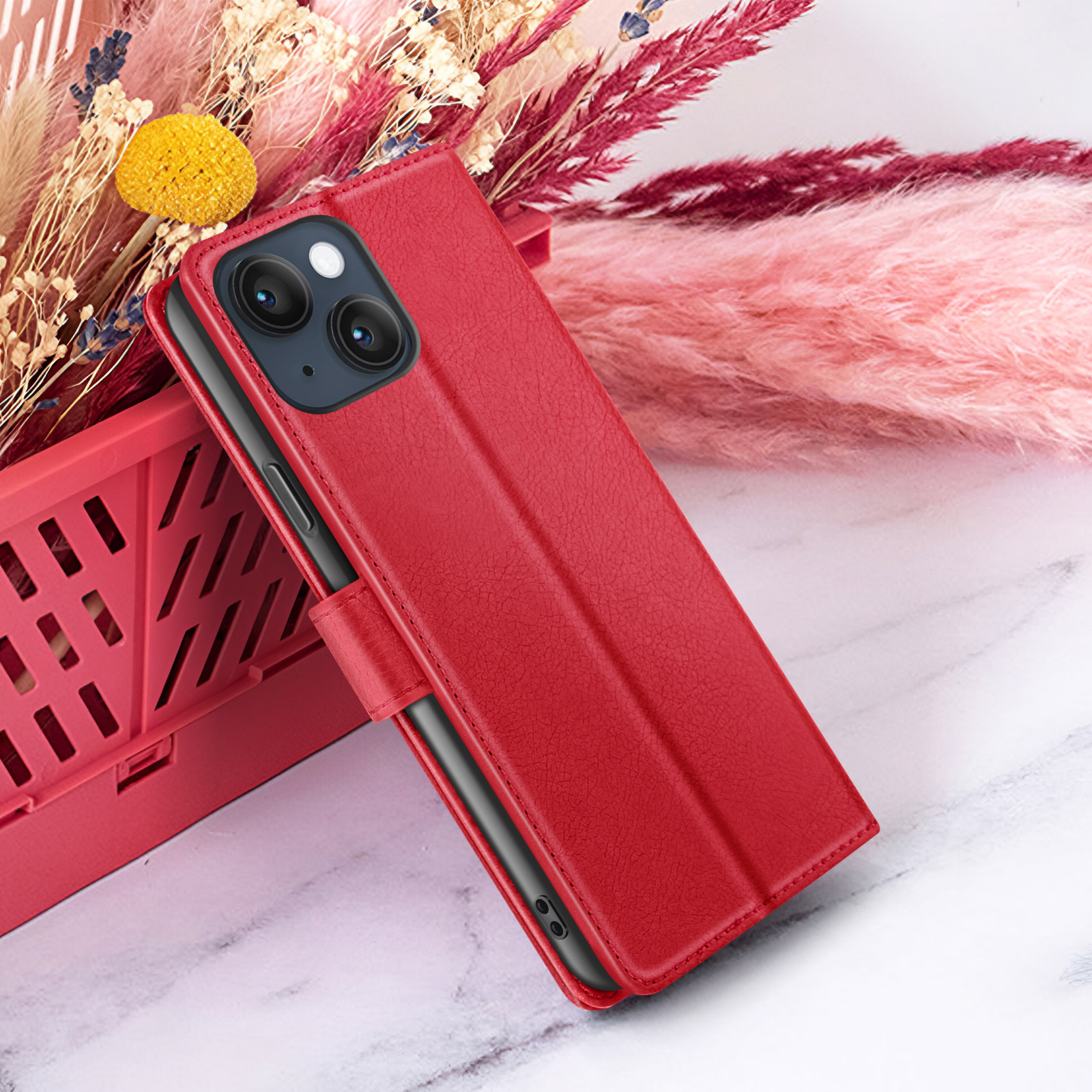 Een rode telefoonhoes wordt gedeeltelijk opengetoond, tegen een achtergrond van roze en beige gedroogde bloemen. De hoes is getextureerd.