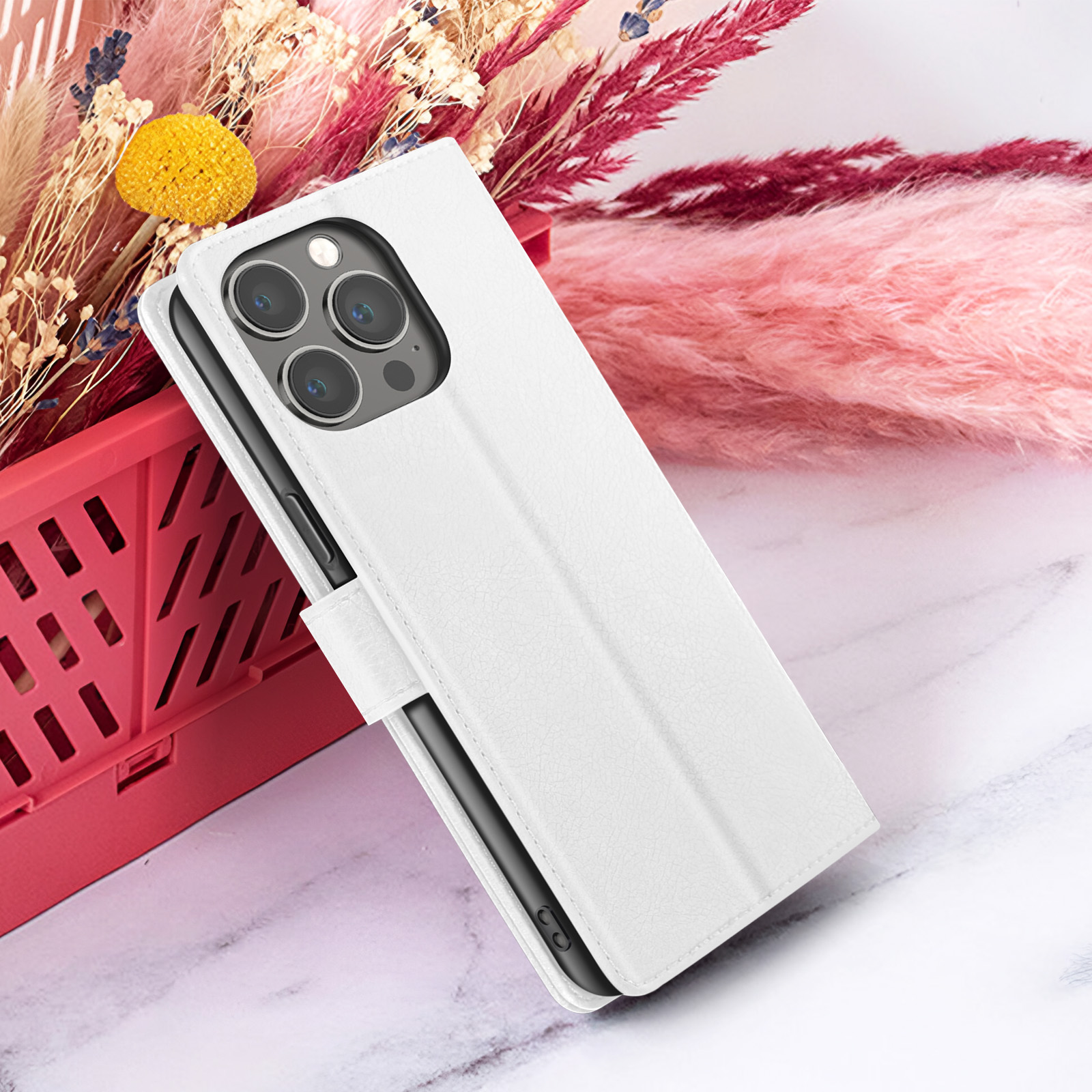Een witte telefoonhoes met een telefoon erin, voor roze en rode bloemen. De achtergrond is een wit marmeren oppervlak.