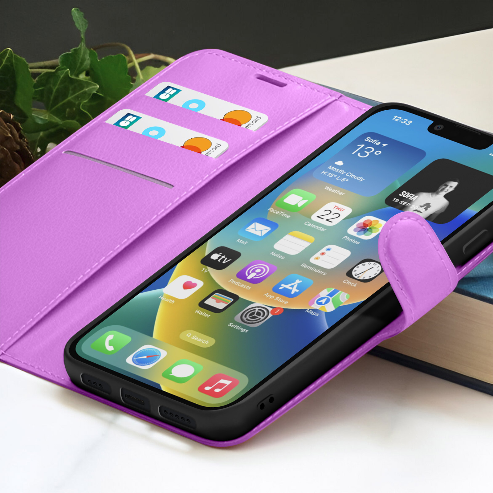 Un smartphone dans un étui violet, affichant son écran avec des icônes d'applications. Cartes de crédit dans une fente. Arrière-plan avec plante et livre.