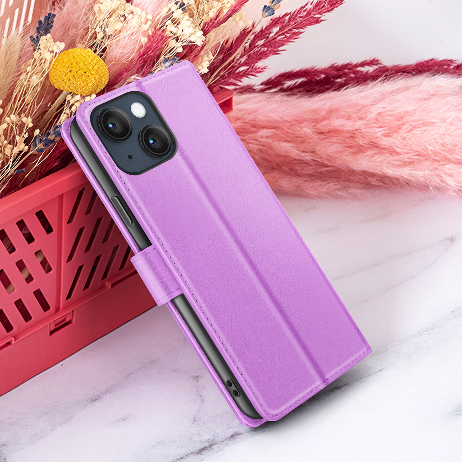 Un étui de téléphone violet est présenté. Derrière, des fleurs séchées roses et beiges, et un panier rouge sont visibles.