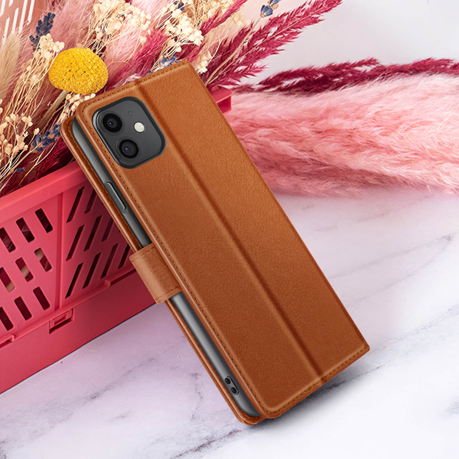 Een bruine leren telefoonhoes met een telefoon erin. Het staat op een marmeren oppervlak met bloemen op de achtergrond.
