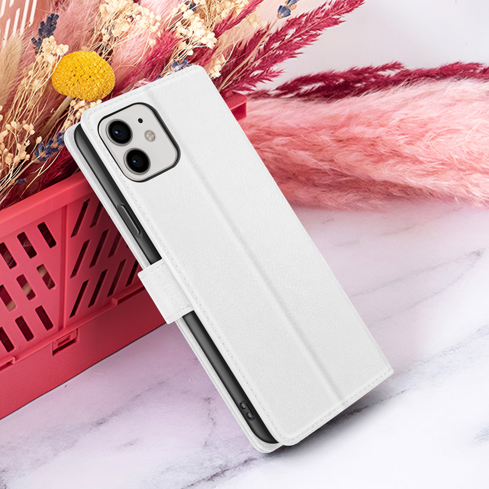 Een witte telefoonhoes met een telefoon erin, tentoongesteld op een marmeren oppervlak met een achtergrond van roze en gedroogde bloemen.