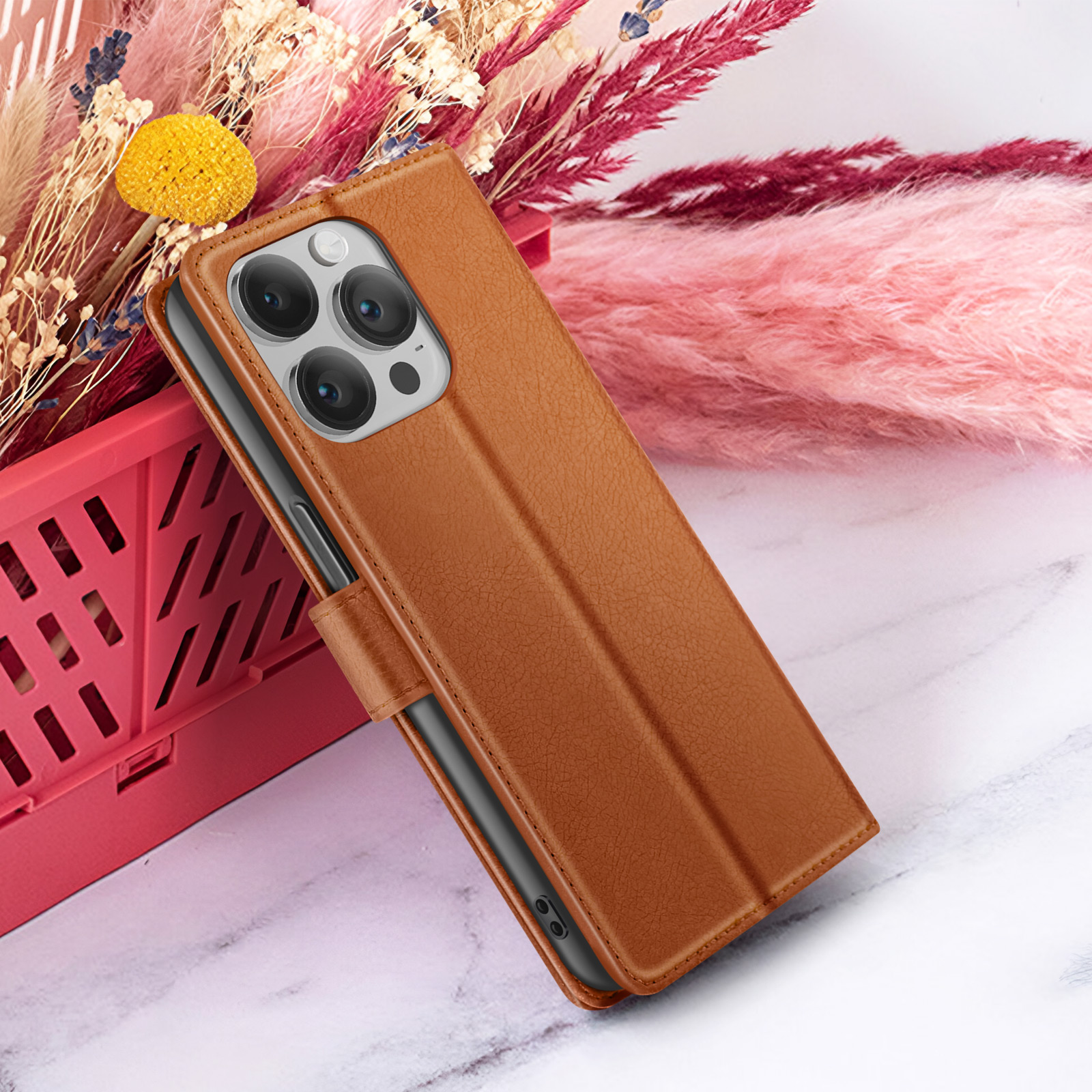 Étui de téléphone en cuir marron avec plusieurs lentilles, posé sur une surface en marbre, avec des fleurs séchées en arrière-plan.
