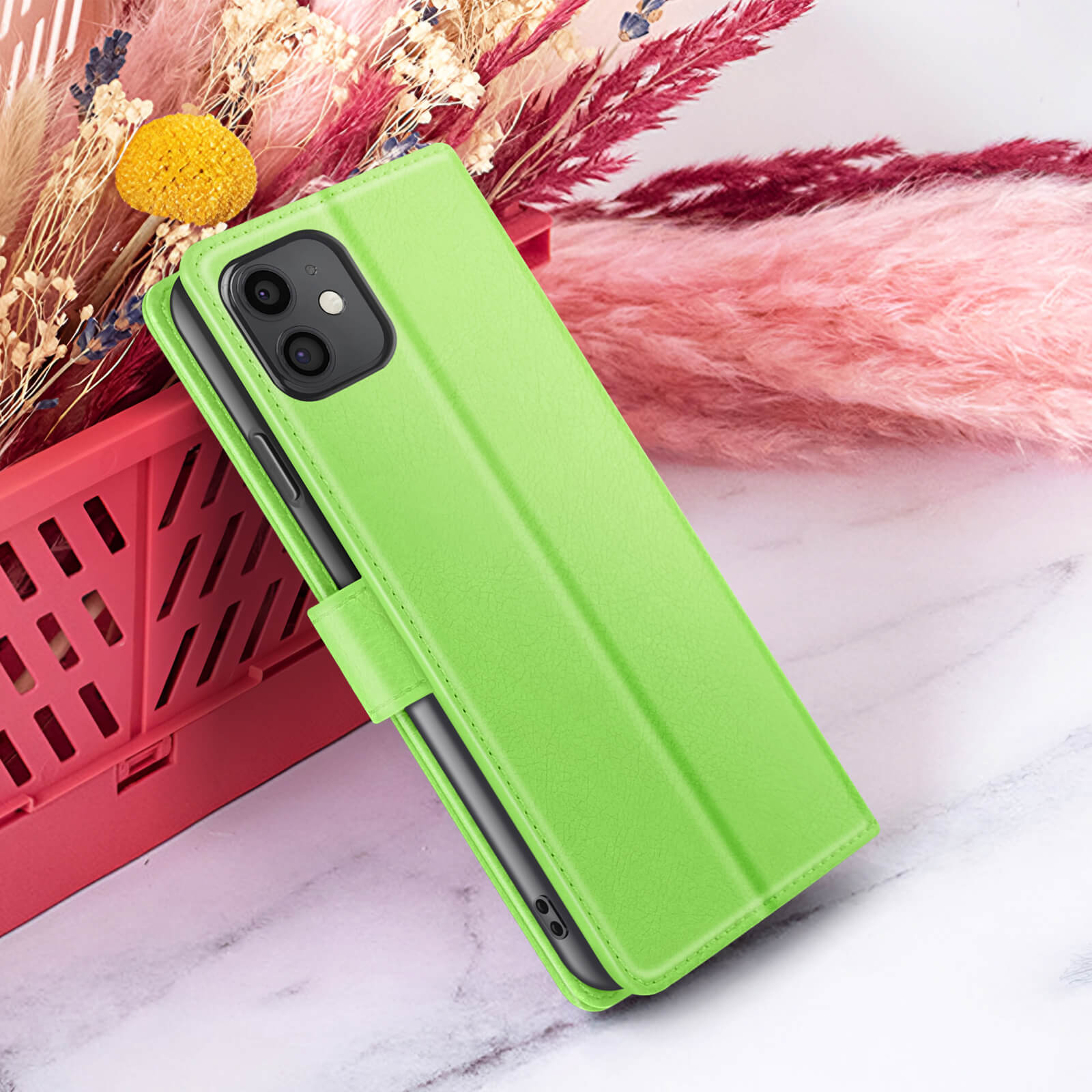 Een groene telefoonhoes is open, rustend op een oppervlak met bloemen op de achtergrond. Een telefoon met twee camera's is zichtbaar.
