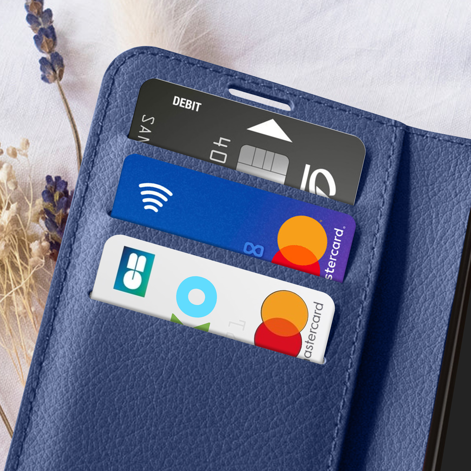 Étui de téléphone bleu avec trois cartes : débit, sans contact et Mastercard. Lavande et tissu blanc en arrière-plan.