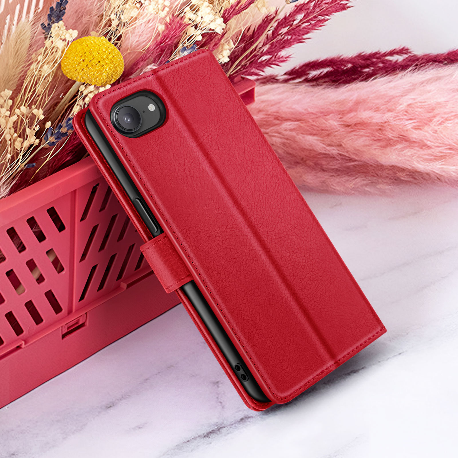Rode telefoonhoes met telefoon, naast roze bloemen en een rode mand, op een wit marmeren oppervlak.