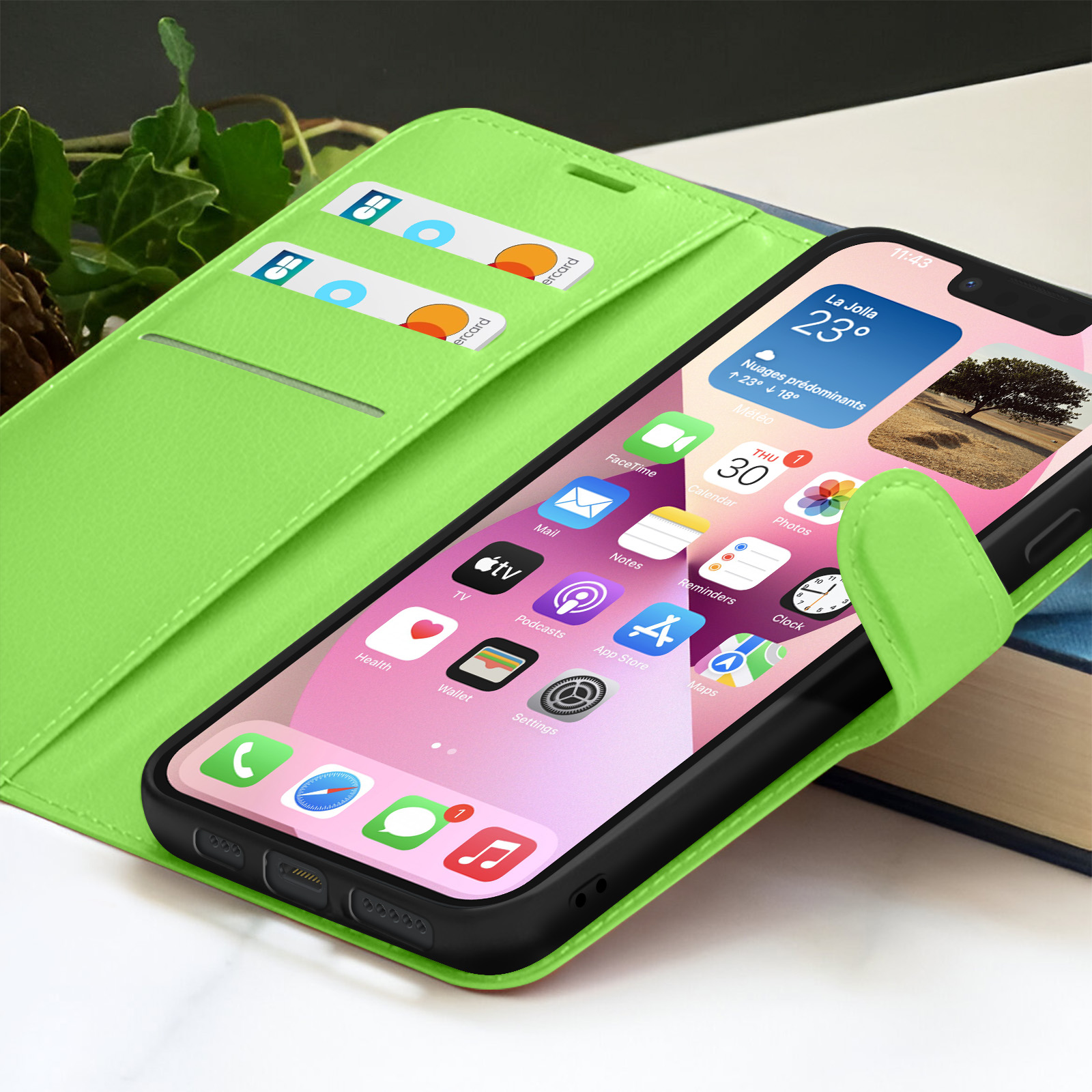 Een iPhone in een groene hoes toont apps en het weer. Creditcards zijn zichtbaar in de sleuven van de hoes. Een boek staat op de achtergrond.