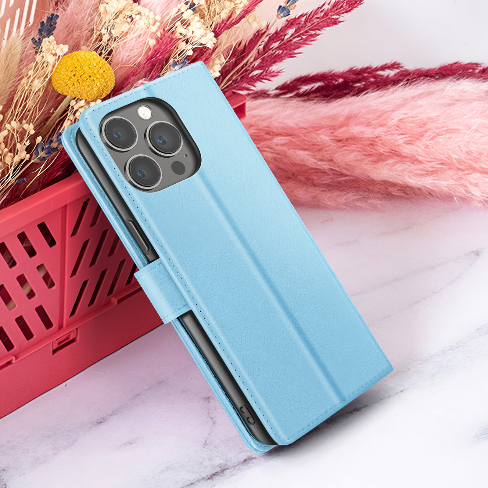 Een blauwe telefoonhoes met een zwarte telefoon erin, voor roze en beige gedroogde bloemen op marmer.