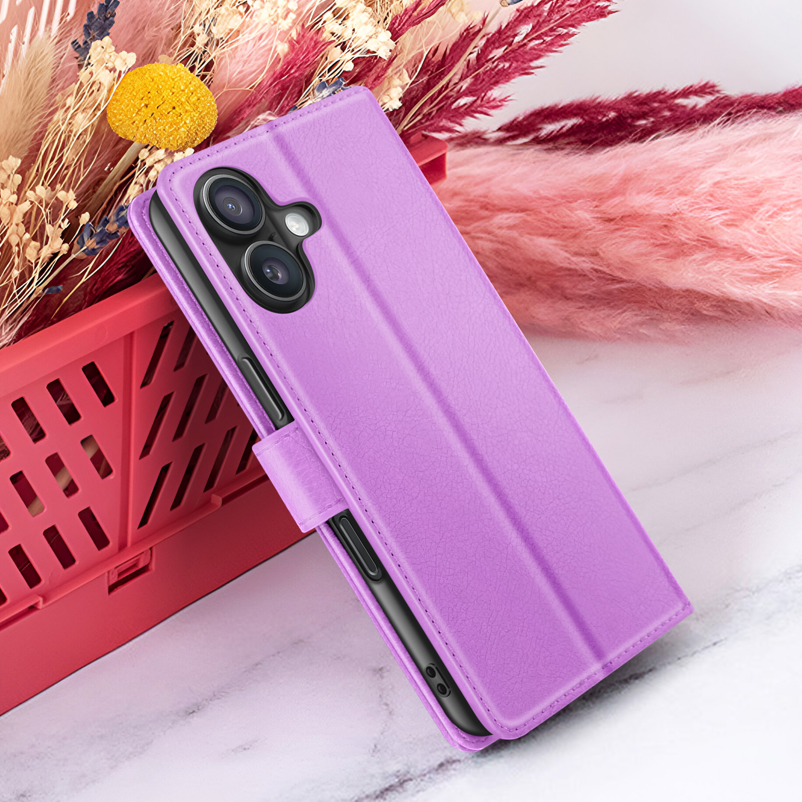 Een paarse telefoonhoes met cameralenzen is open. Het staat naast roze en rode decoratieve planten, in een rode mand op een marmeren oppervlak.