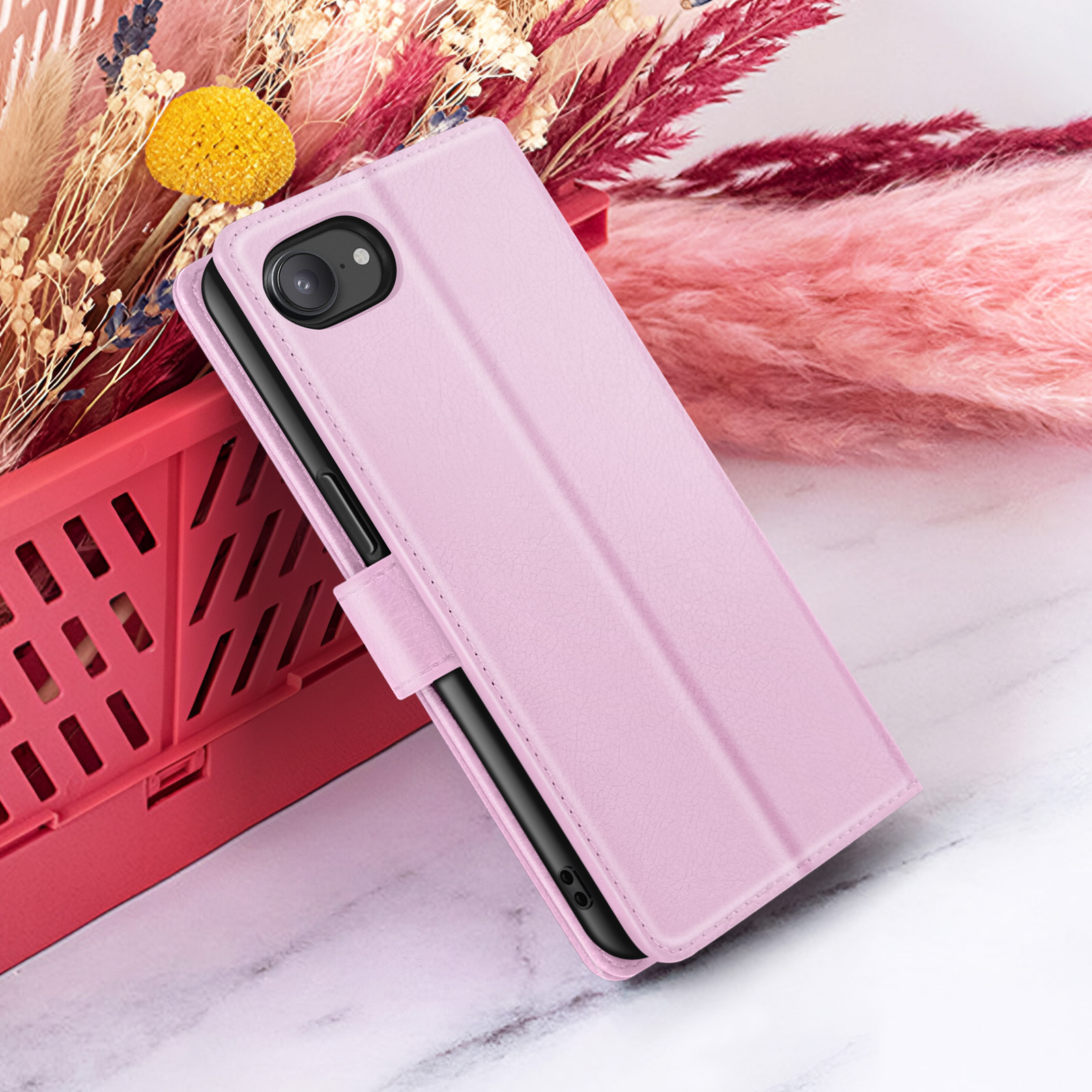 Een roze telefoonhoesje met telefoon, tegen een roze bak. Bloemelementen op de achtergrond.