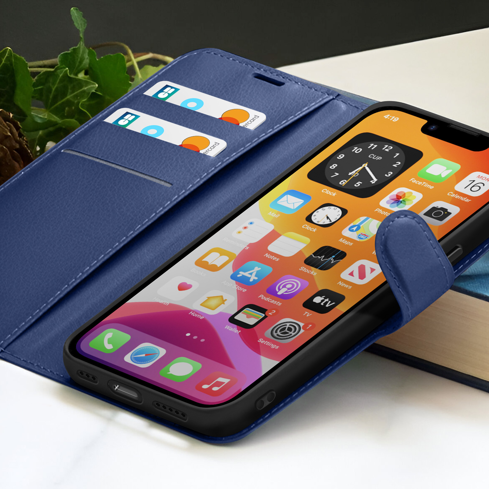 Een smartphone in een blauwe hoes geeft app-iconen weer. Twee creditcards zitten in een sleuf. De achtergrond heeft bladeren en een boek.