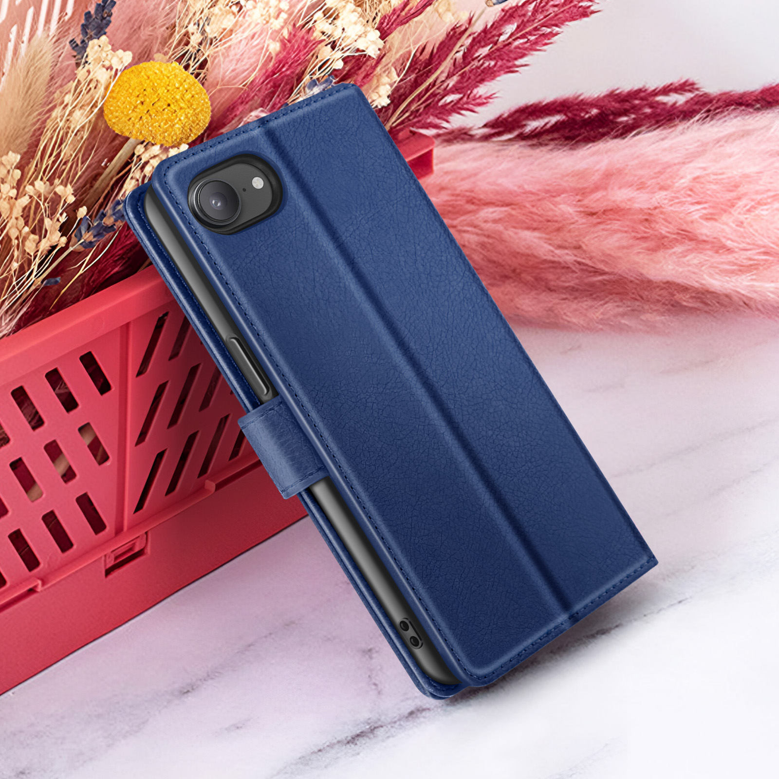 Een blauwe telefoonhoes is open, rustend op een rode mand. Gedroogde bloemen van roze, beige en geel op de achtergrond.