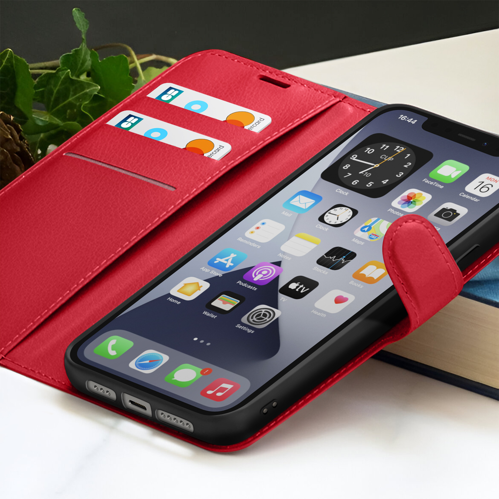 Een rode telefoonhoes bevat een zwarte iPhone met apps. Creditcards in de sleuven en een boek op de achtergrond.