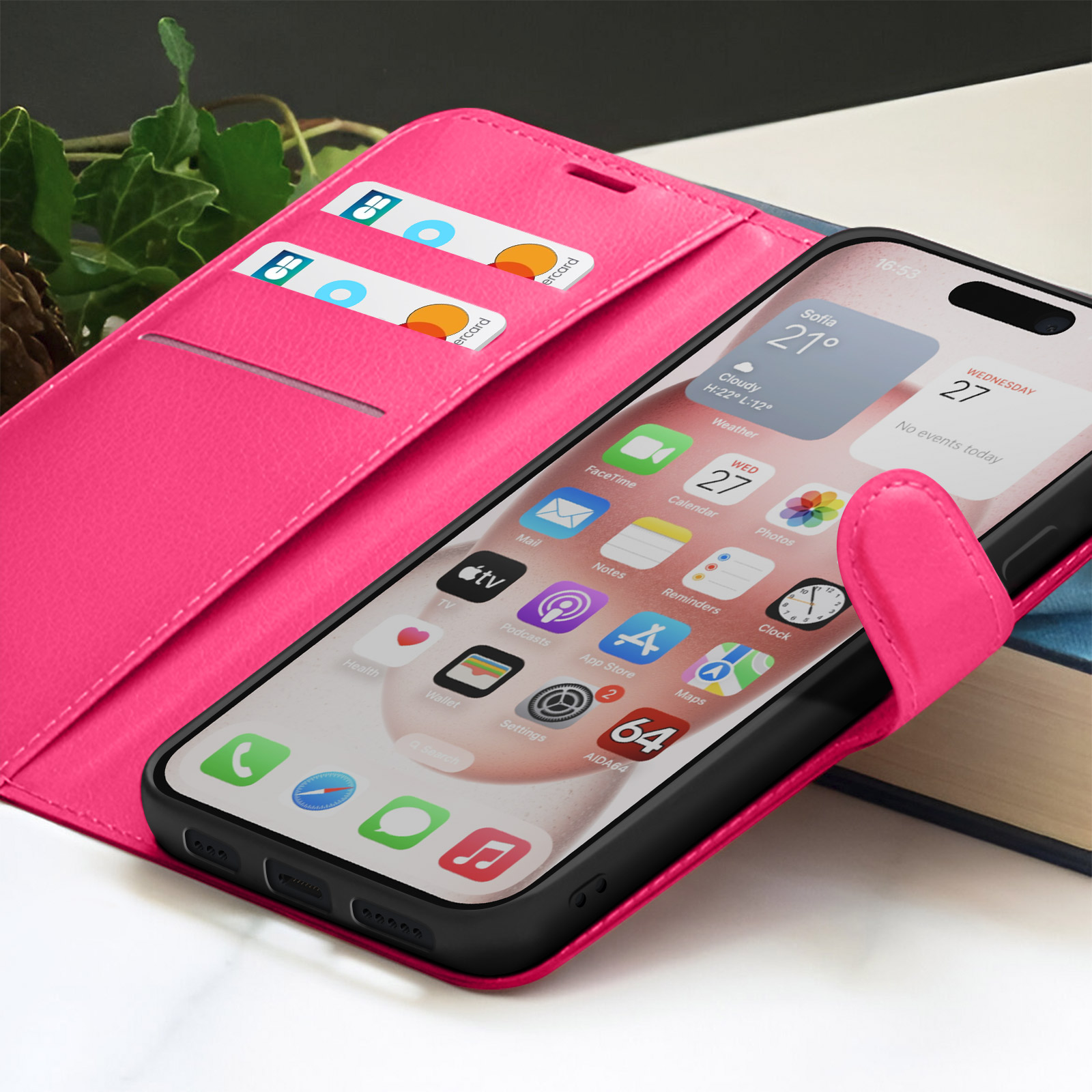 Un étui de téléphone rose contenant un téléphone affichant des applications. Des cartes de crédit sont visibles dans l'étui. Fond avec des livres et feuillage.