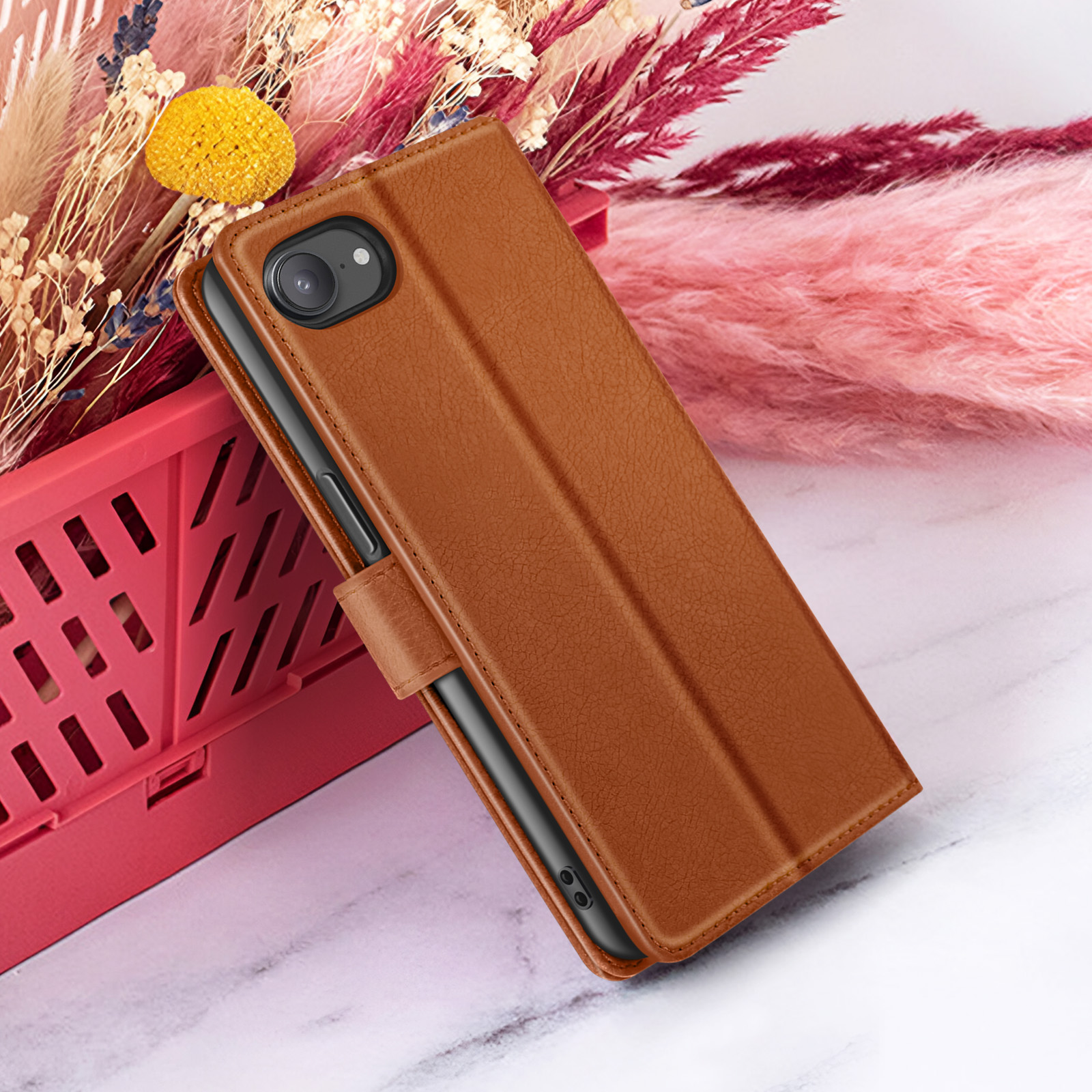 Bruine leren telefoonhoes met camera, rustend op een rode mand met bloemen op de achtergrond.