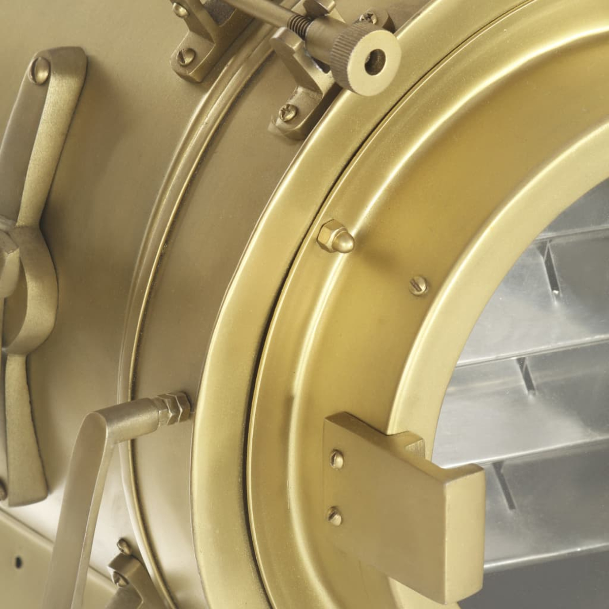 Nahaufnahme eines messingfarbenen Scheinwerfers mit runder Linse. Der Scheinwerfer hat verschiedene mechanische Teile und einen Griff. Der Hintergrund ist unscharf.