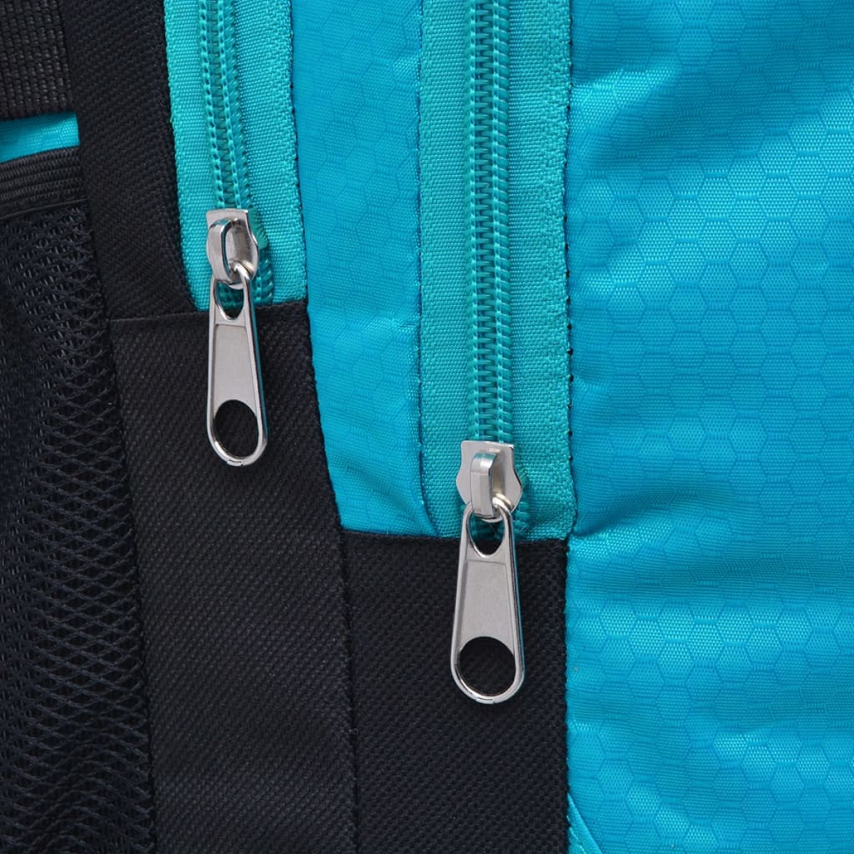 Nahaufnahme eines Rucksacks mit zwei silbernen Reißverschlüssen auf türkisfarbenem und schwarzem Stoff.