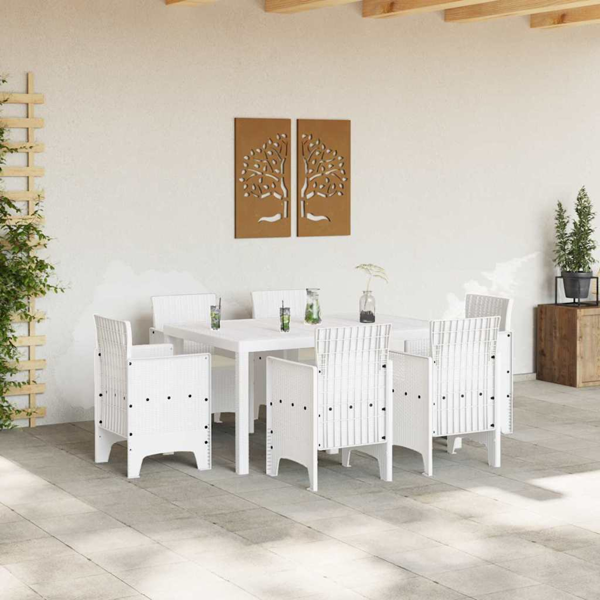 Set da pranzo all'aperto con tavolo e sedie bianche. Pannelli decorativi ad albero sulla parete. Piante in vaso e bicchieri sul tavolo.
