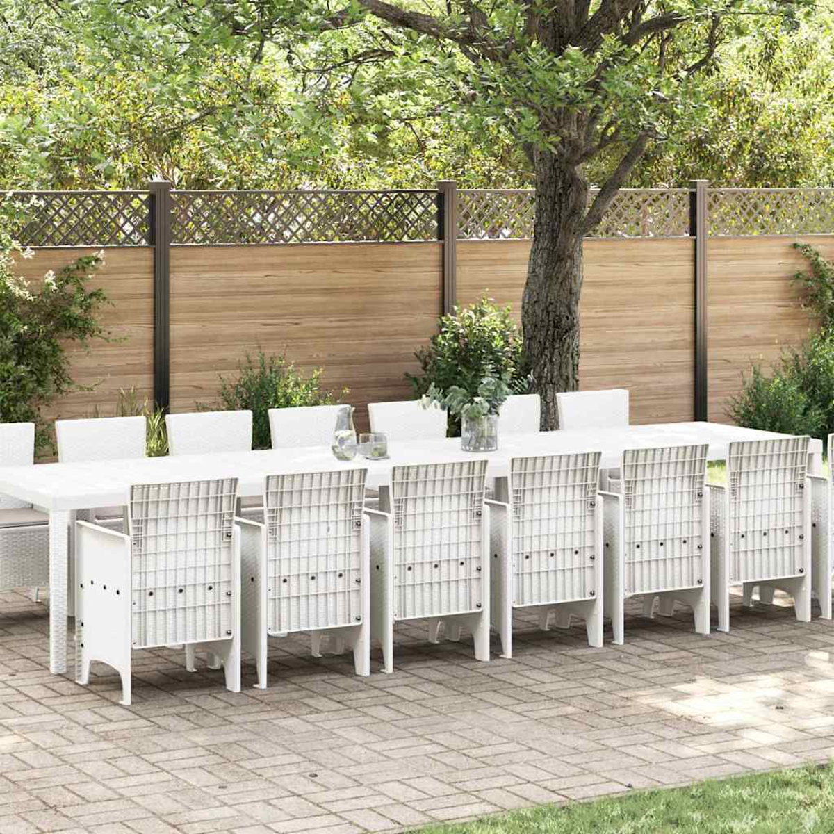 Szene im Freien mit einem weißen Tisch und Stühlen auf einer Ziegelterrasse, Bäumen im Hintergrund und einem Holzzaun.