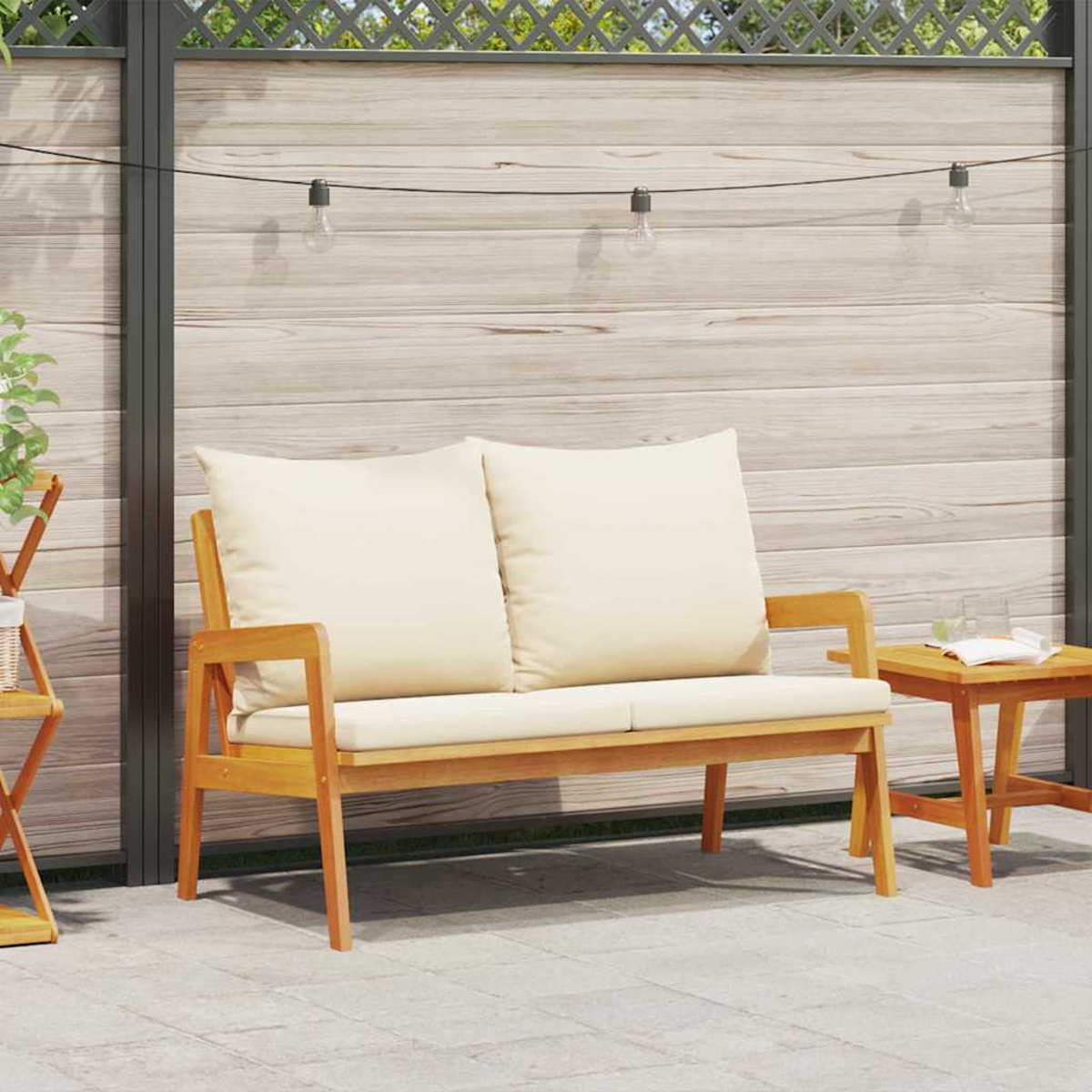 Ein hölzernes Outdoor-Sofa mit cremefarbenen Kissen steht auf einer Terrasse. Daneben steht ein kleiner Beistelltisch mit Glas und Buch.