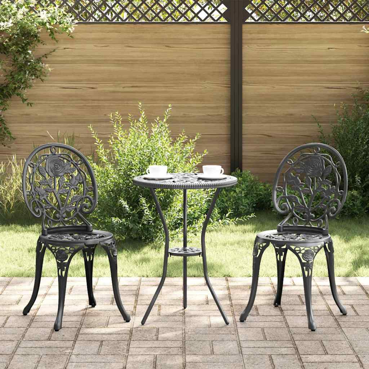 Ein Terrassenset mit zwei Stühlen und einem Tisch. Die Stühle und der Tisch sind aus verziertem schwarzem Metall.
