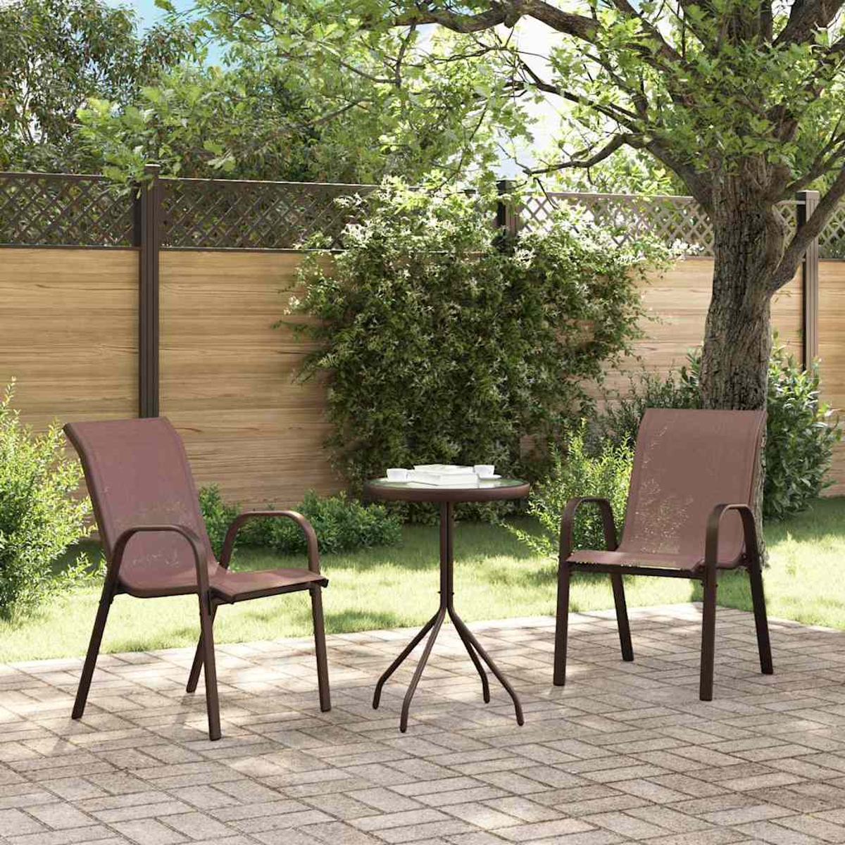 Zwei braune Stühle und ein kleiner Tisch auf einer gepflasterten Terrasse. Dahinter ein Holzzaun und Bäume. Sonnige Szene im Freien.